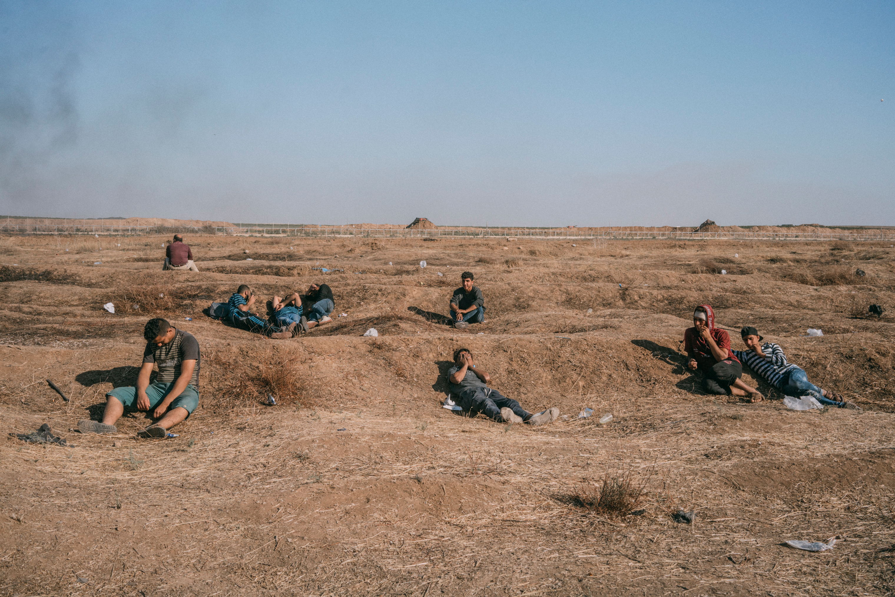 Palestinians sit along the Gaza-Israel border as smoke wafts in the distance. (Emanuele Satolli for TIME)