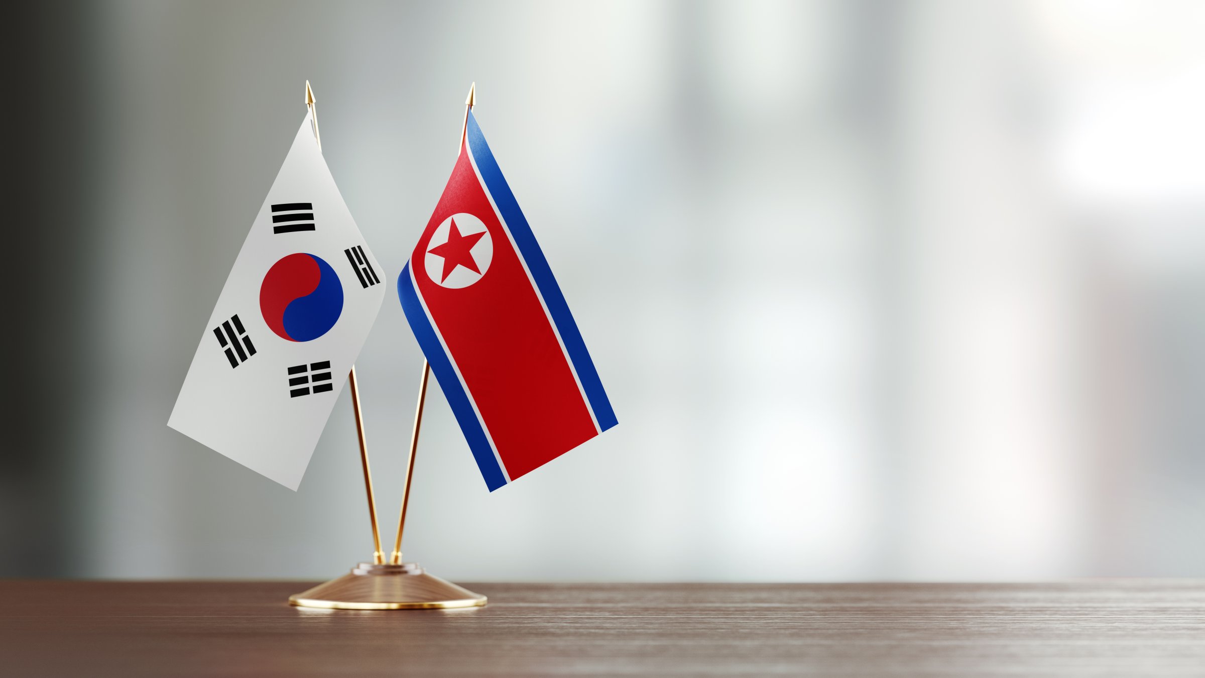 South Korean And North Korean Flag Pair On A Desk Over Defocused Background