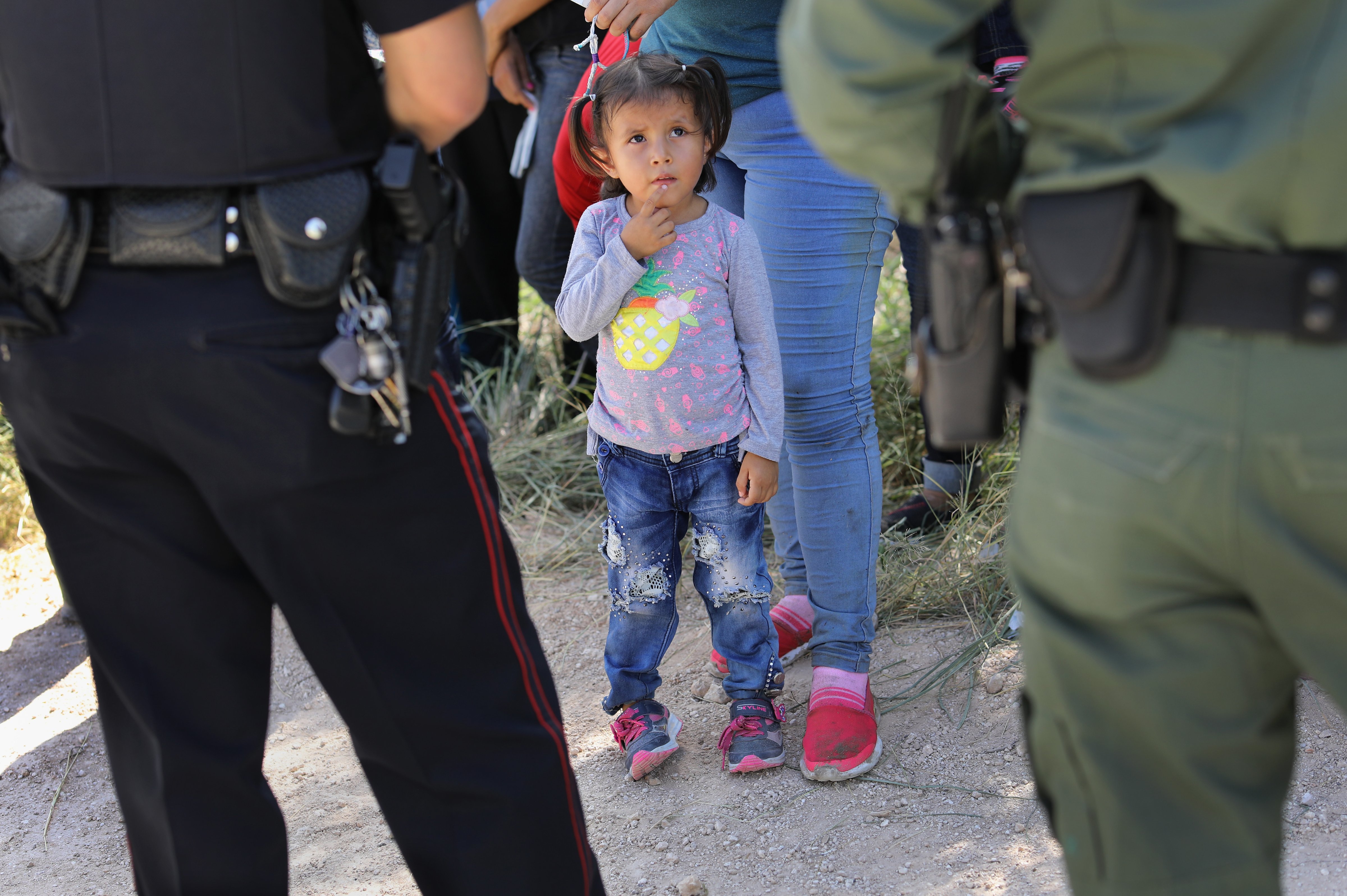 A Mission Police Dept. officer (L), and a U.S. Border Patrol agent watch over a group of Central American asylum seekers before taking them into custody on June 12, 2018 near McAllen, Texas (John Moore&mdash;Getty Images)