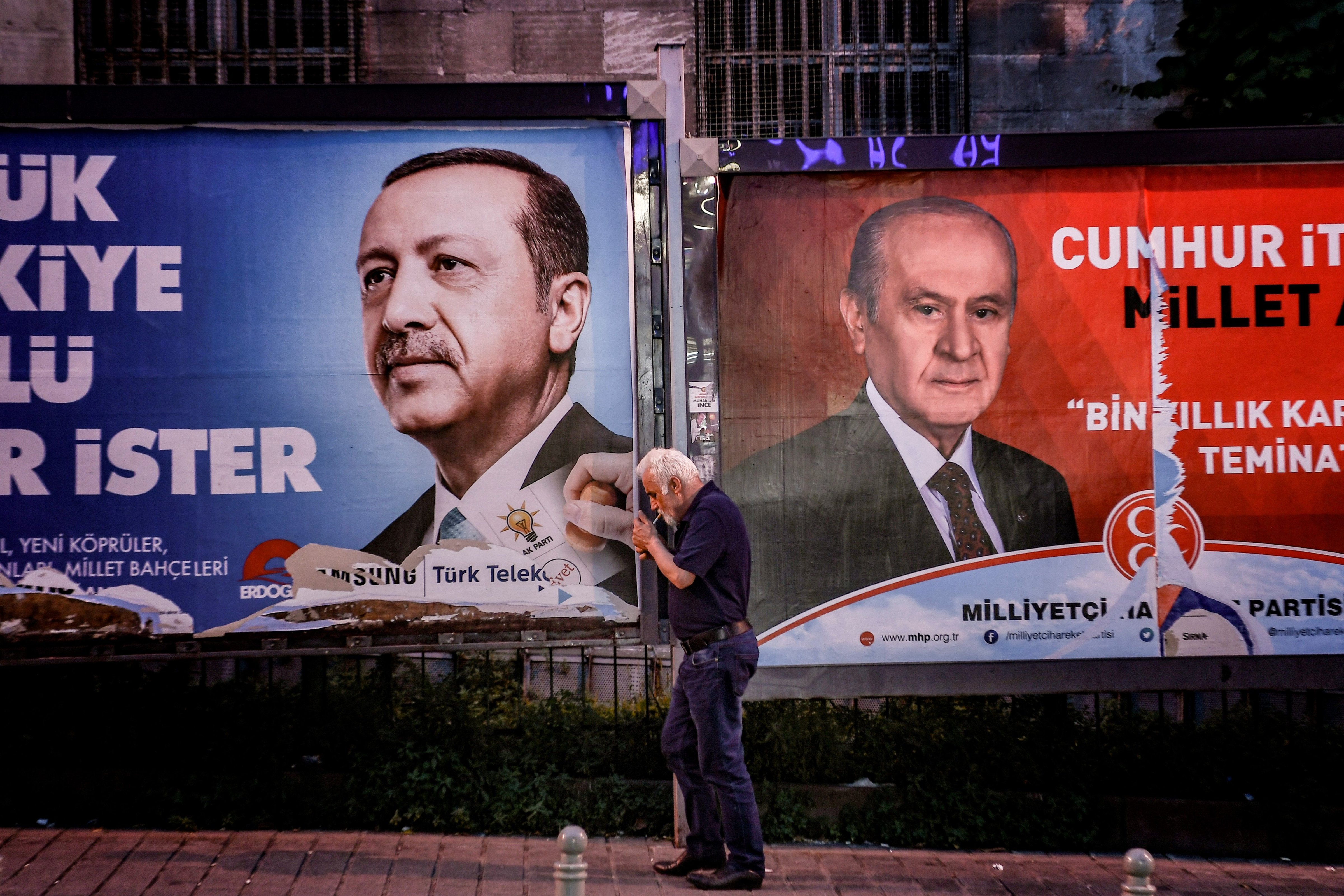A pedestrian lights a cigarette as he walks past in banners with portraits of Turrkish President Recep Tayyip Erdogan (L) and the leader of Nationalist Movement Party (MHP) Devlet Bahceli in Istanbul on June 19, 2018. (Aris Messinis—AFP/Getty Images)