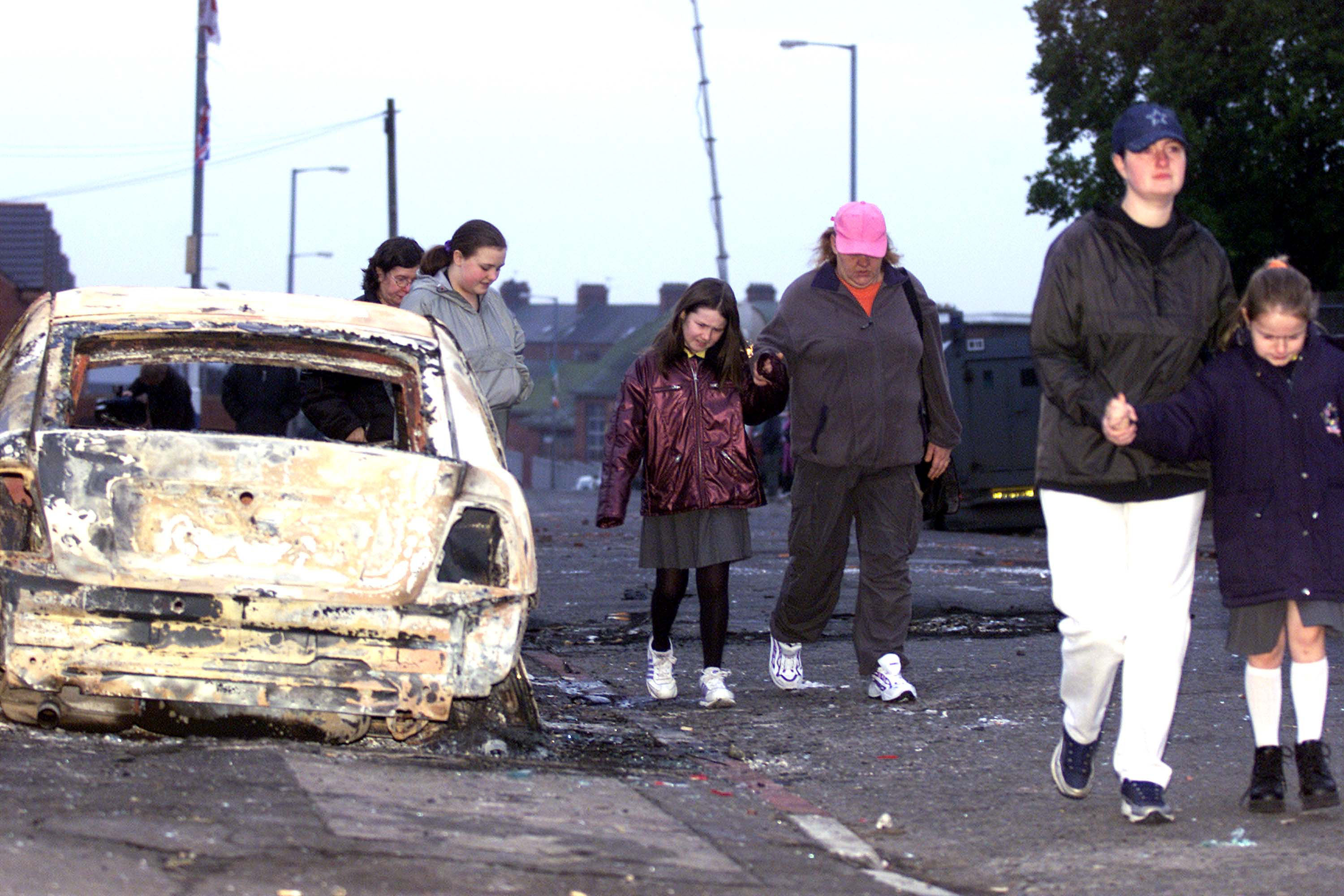 Local residents of the Glenbryn area in North Belfast walk past burnt-out remains of an armored police car following overnight rioting between Nationalists and Loyalists crowds January 10, 2002 in Belfast, Northern Ireland. Rioting erupted as Catholic parents picked up their children from the Holy Cross girls'' primary school. (Cathal McNaughton—Getty Images)