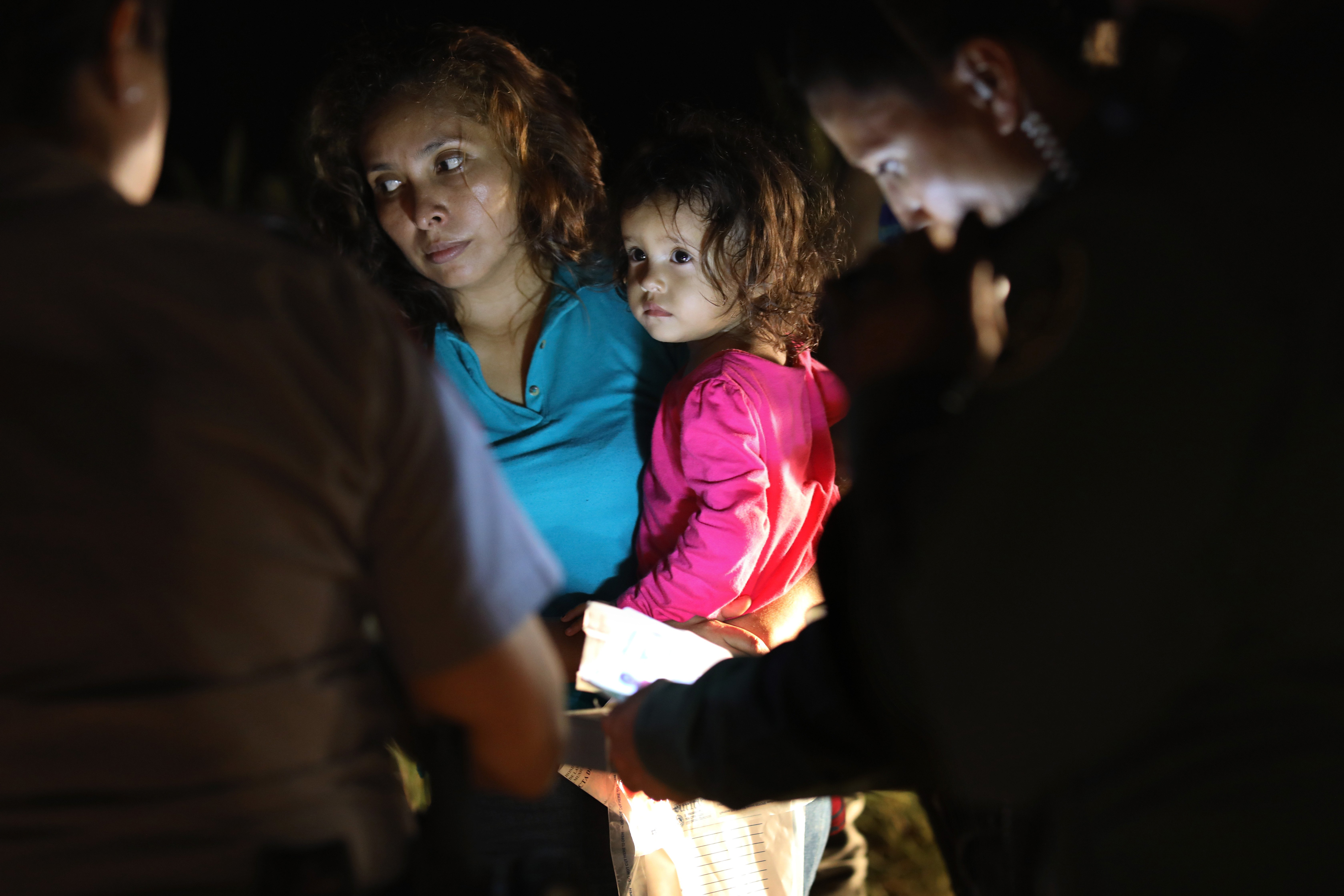 A Honduran mother holds her two-year-old as U.S. Border Patrol as agents review their papers near the U.S.-Mexico border in McAllen, Texas on June 12, 2018. The asylum seekers had rafted across the Rio Grande from Mexico and were detained by U.S. Border Patrol agents before being sent to a processing center for possible separation. (John Moore—Getty Images)