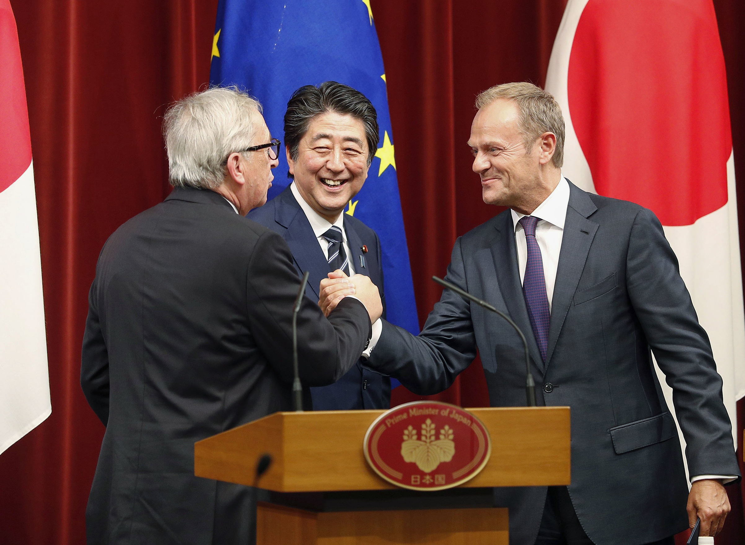 European Council President Donald Tusk (R) and European Commission President Jean-Claude Juncker (L), alongside Japanese Prime Minister Shinzo Abe, shake hands at Abe's office in Tokyo on July 17, 2018, after they signed a free trade deal with Japan. (Kyodo News/Sipa USA)