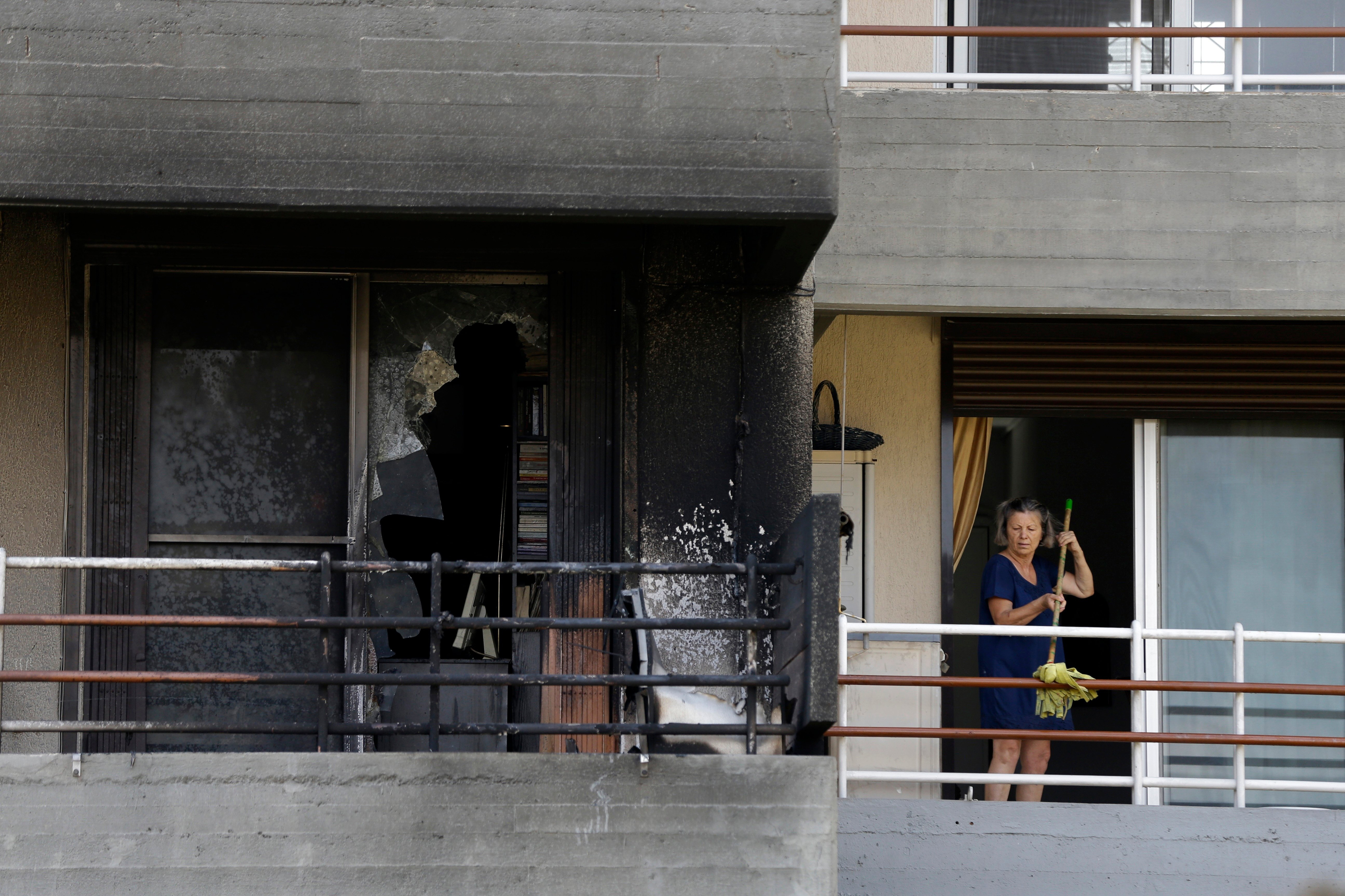 A woman cleans her balcony next to a burned apartment in Mati on July 25, 2018. (Thanassis Stavrakis—AP/Shutterstock)