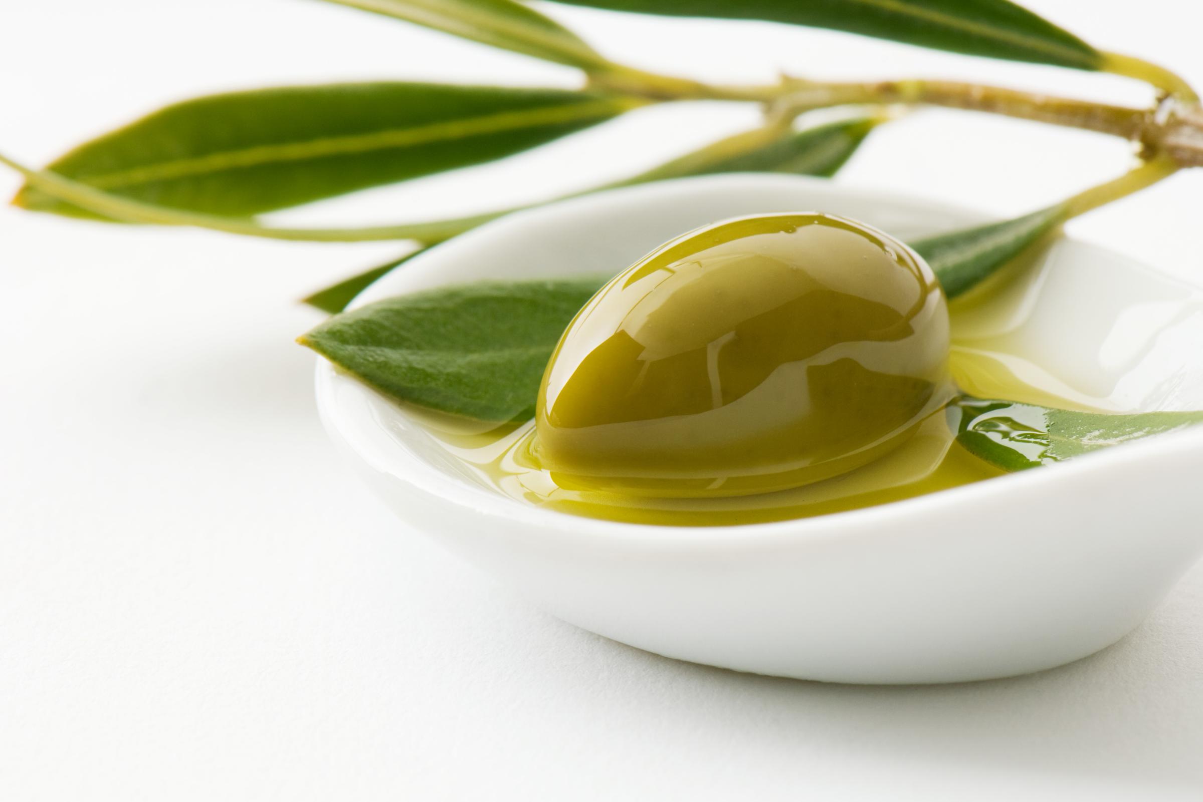 Green olive and sprig of leaves in small dish of olive oil, close-up