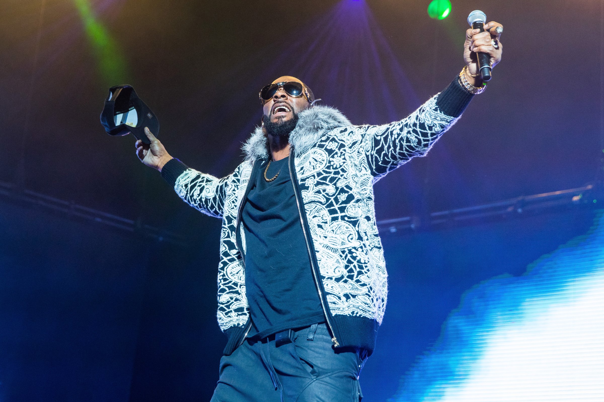 R. Kelly wears a fuzzy jacket and raises his arms to the side during concert
