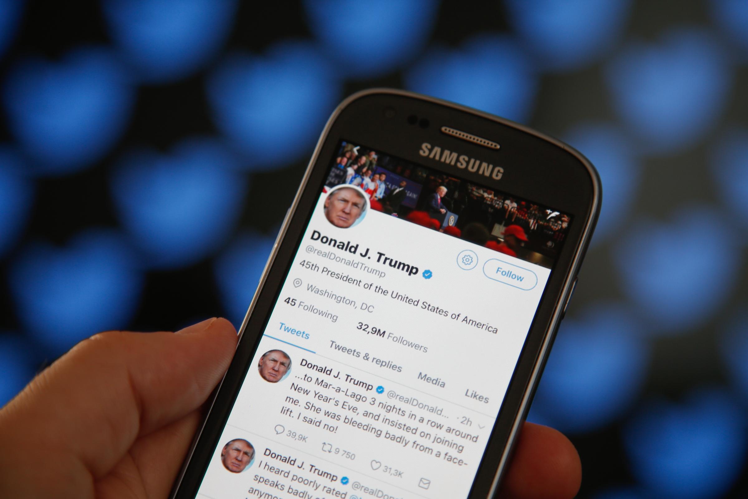 Trump's twitter timeline in front of a screen with the Twitter logo in a patten