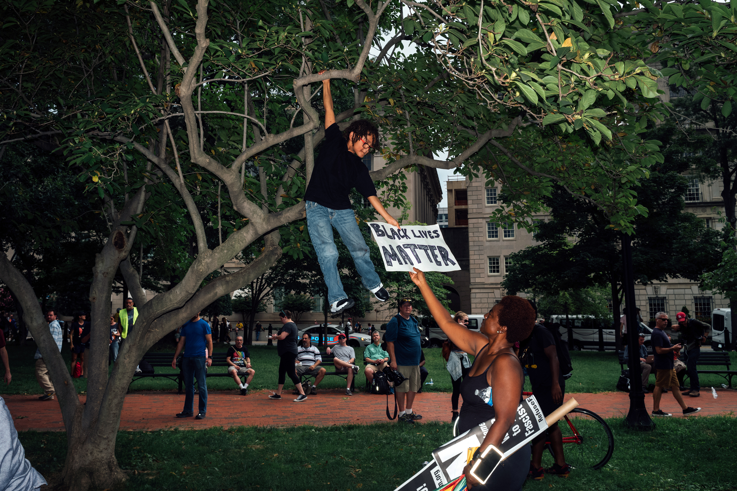 A woman hands a Black Lives Matter sign back to a young boy, who was readjusting his position in a tree, at Lafayette Square. (Daniel Arnold for TIME)