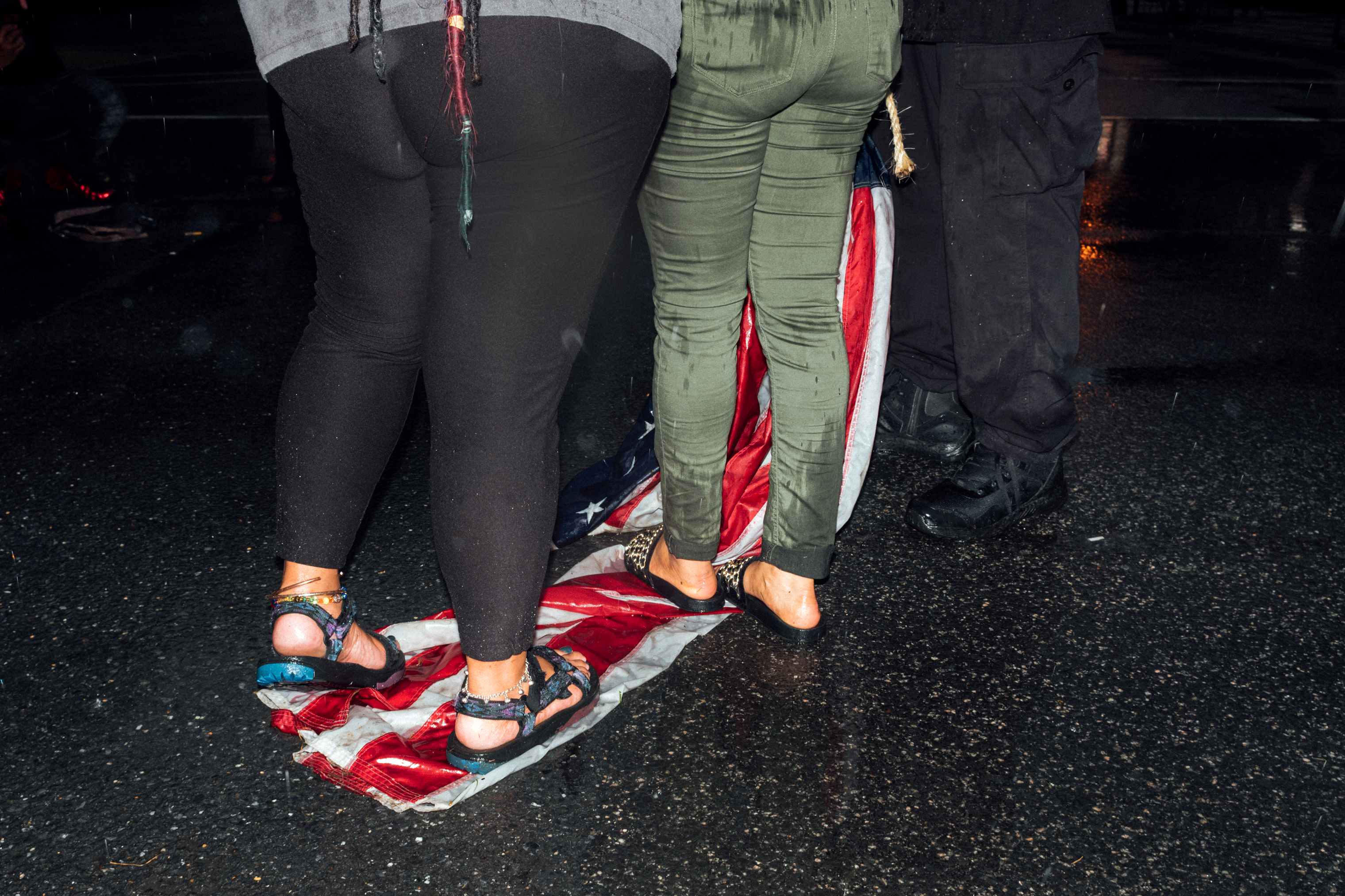 Two women stand on an American flag that throughout the day had been hung at various locations by a man aiming to call attention to racial injustices. (Daniel Arnold for TIME)