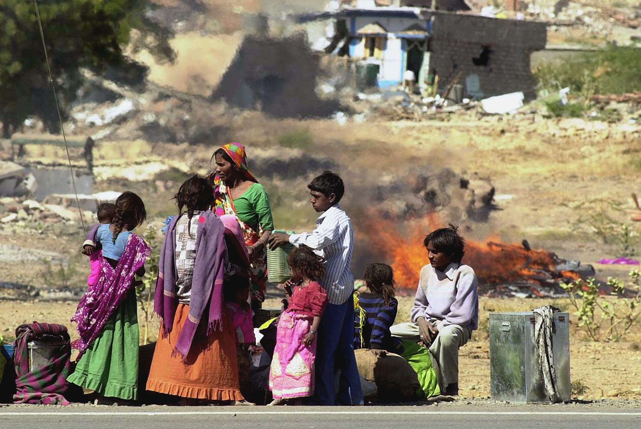 A homeless family waits for a vehicle on Jan. 27, 2001 against a backdrop of ruined houses and a funeral pyre, in the village of Boundi in Bhuj district in Gujarat. (Arko Datta—AFP/Getty Images)