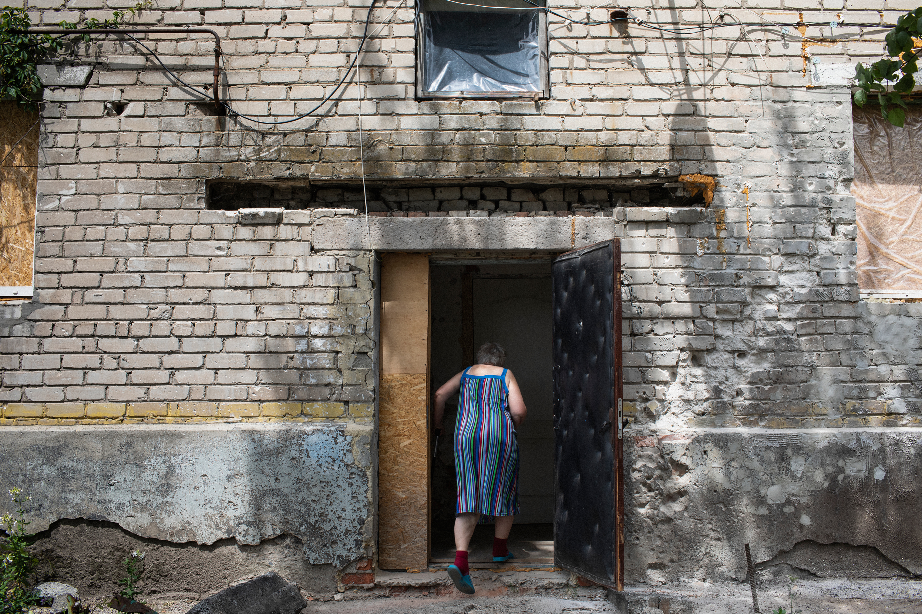 A woman walks into a home that has sustained shell damage in the village of Novoluganskoe. Eastern Ukraine is full of pensioners who have stayed behind, often due to a lack of money or physical strength. (Anastasia Taylor-Lind for eyeWitness)