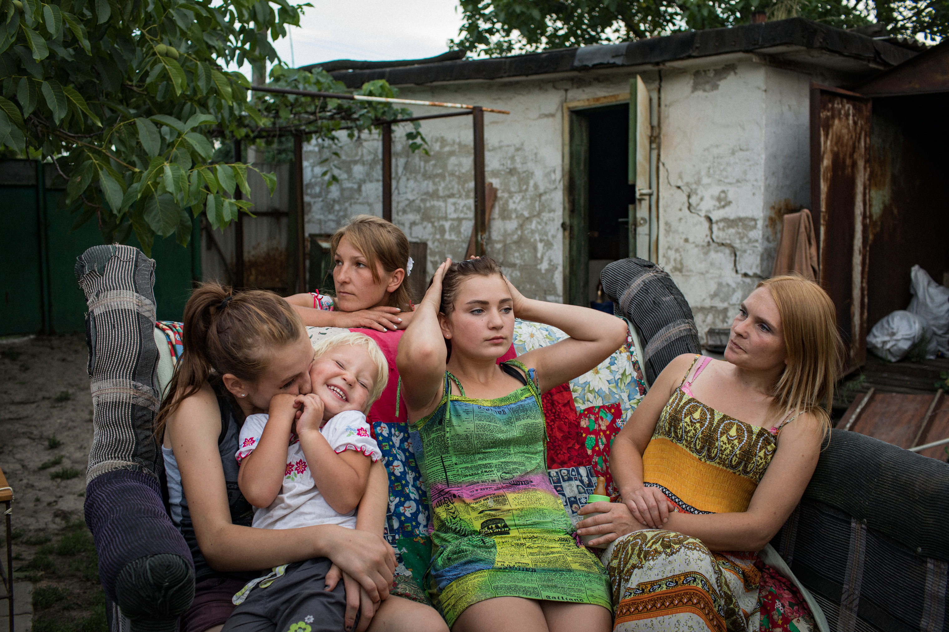 Aleksandra Mountyan, Miroslava Grinik, Olga Grinik, Victoria Mountyan and Valentina Mountyan—all members of an extended family—hang out in the backyard of Olga’s house, located 50 meters from a Ukrainian military position in old Avdeevka. People may appear relaxed to the sounds of shelling and gunfire, but it’s an illusion: they listen to determine the degree of danger. Everyone knows the safest place in their home. (Anastasia Taylor-Lind for eyeWitness)