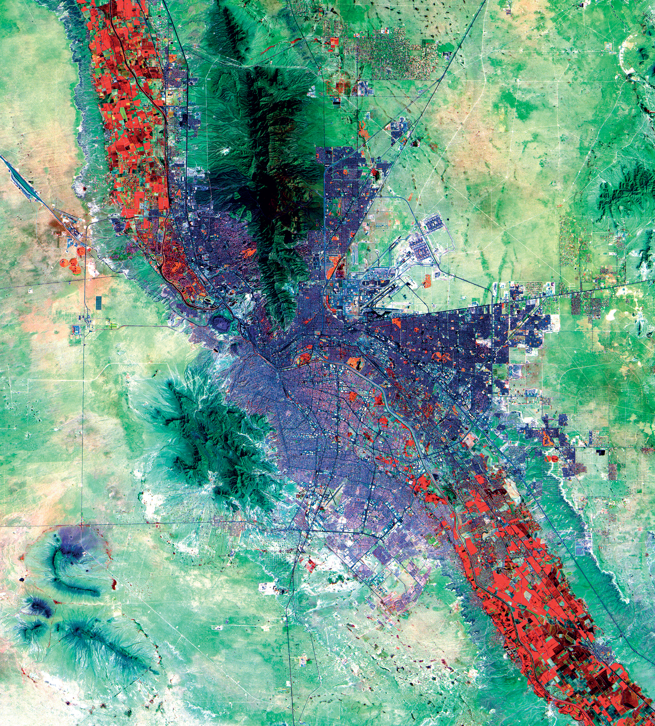 <strong>El Paso, Texas, U.S. and Ciudad Juárez, Chihuahua, Mexico</strong> <em>1:271,000</em> The two cities appear in purple along the Mexican and U.S. border. El Paso, Texas, is concentrated between the border and the Franklin Mountains (in dark green). Ciudad Juárez, Chihuahua, is south of the border. The differences in the two city’s street layouts, infrastructure, building densities and urban materials are clearly evident and shown as various shades of purple. Highly vegetated riparian areas appear in red. (Landsat OLI/TIRS)