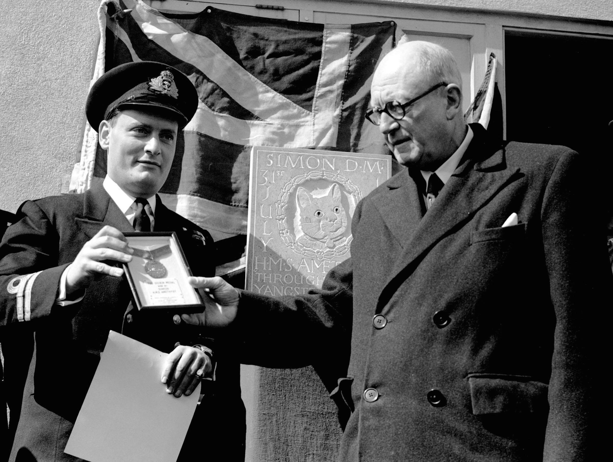 Alderman W. Harry Taylor with Lieutenant Geoffrey Weston (L) who assumed command of the frigate Amethyst, unveiling a plaque in memory of the ship's cat Simon, in Plymouth, after the cat received the Dickin Medal, for catching rats and protecting food supplies during the time the ship was trapped by the Chinese (PA Images / Getty Images)