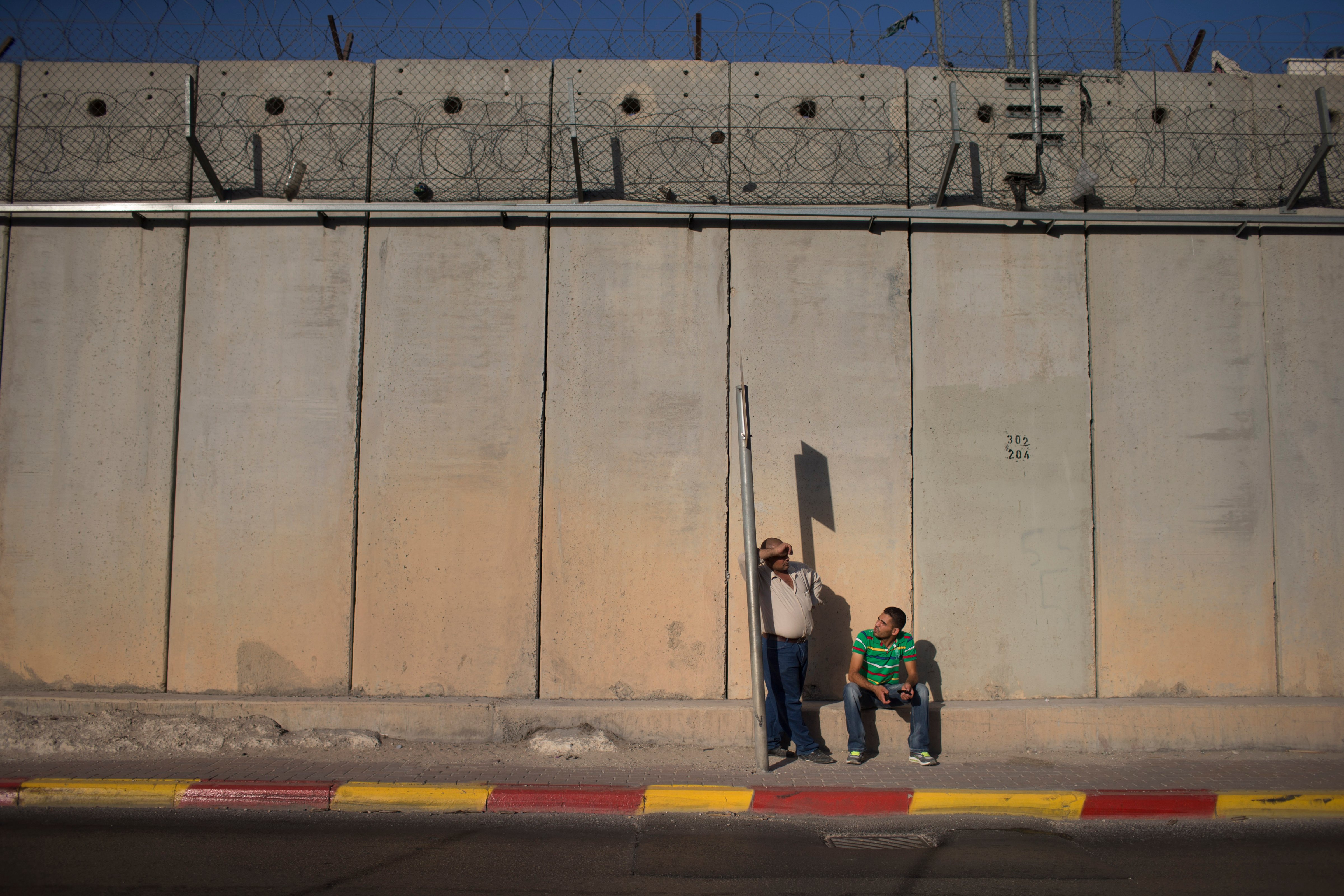 Palestinian men wait for a bus along the Israeli West Bank barrier on the outskirts of Jerusalem on September 12, 2013 in Aram, West Bank. (Uriel Sinai—Getty Images)