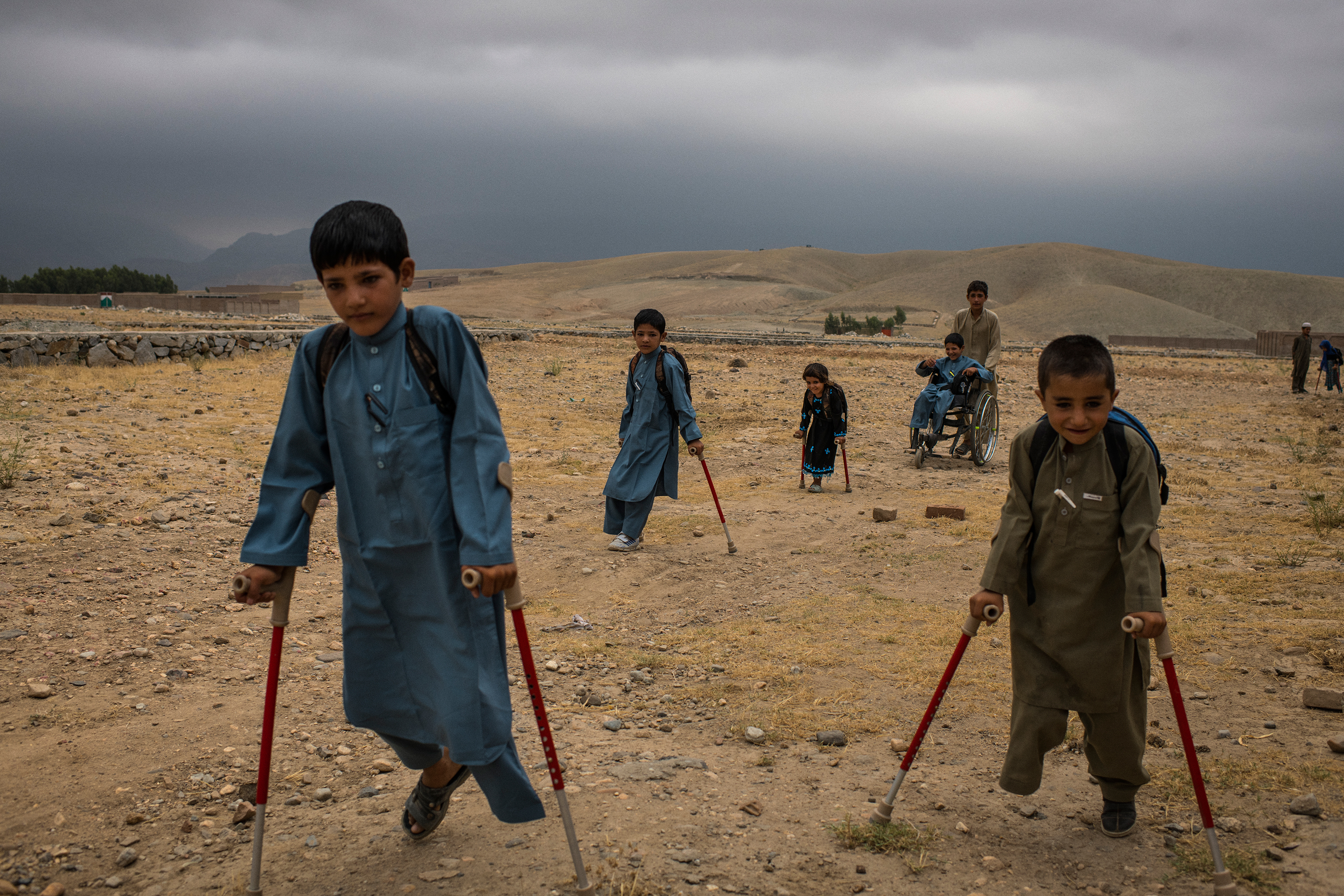 From left, Bashir, Mangal, Marwa, Abdul Rashid (in wheelchair), Aman and, in the distance, Rabia are helped by their cousins on July 23 to a nearby house where they attended school while recovering. (Andrew Quilty for TIME)