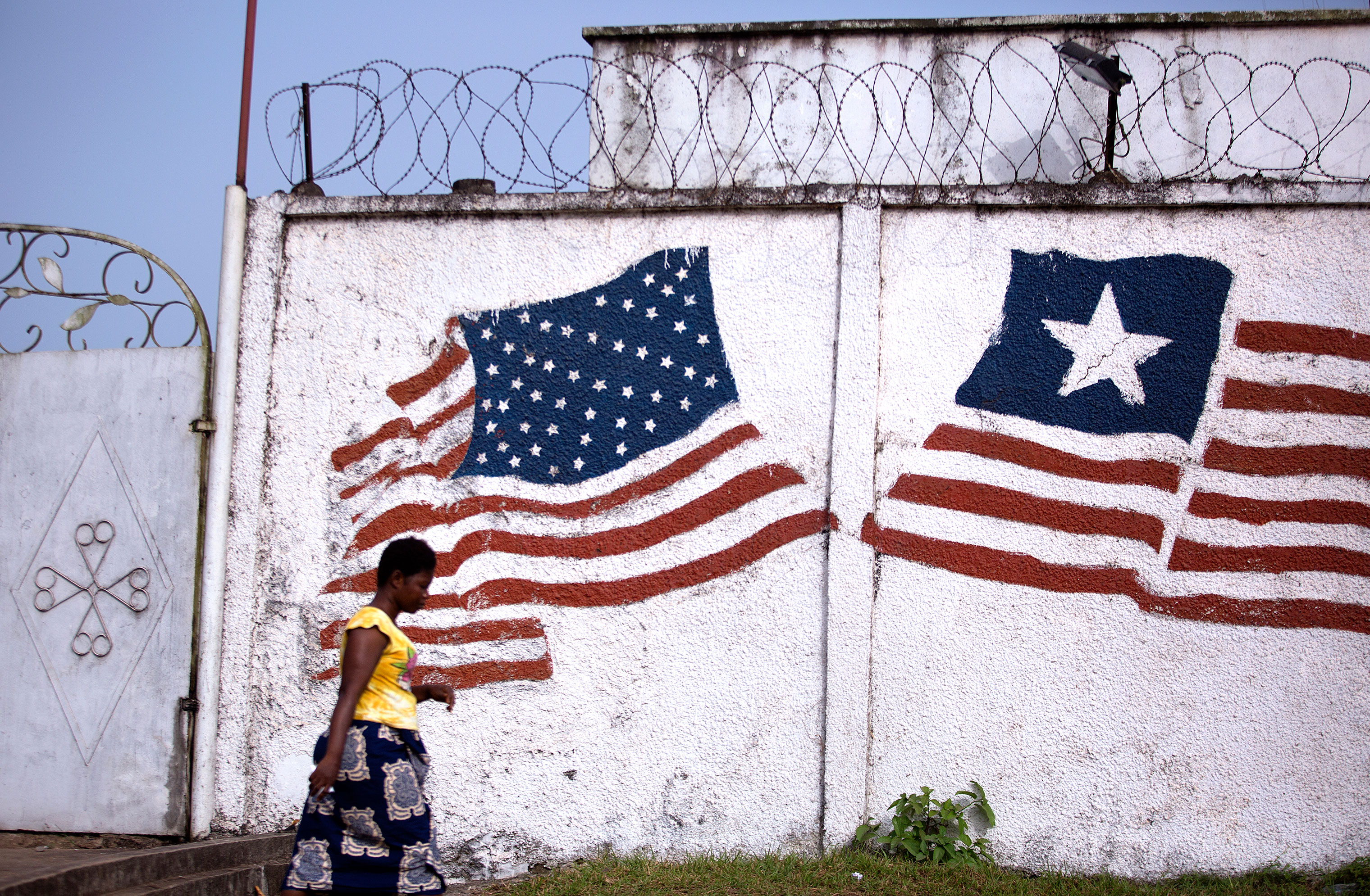 A woman in Monrovia walks past a mural of the Liberian and American flags. Liberia was formed by the American Colonization Society, an organization that resettled free African Americans and freed slaves. (Kathleen Flynn, special to ProPublica)