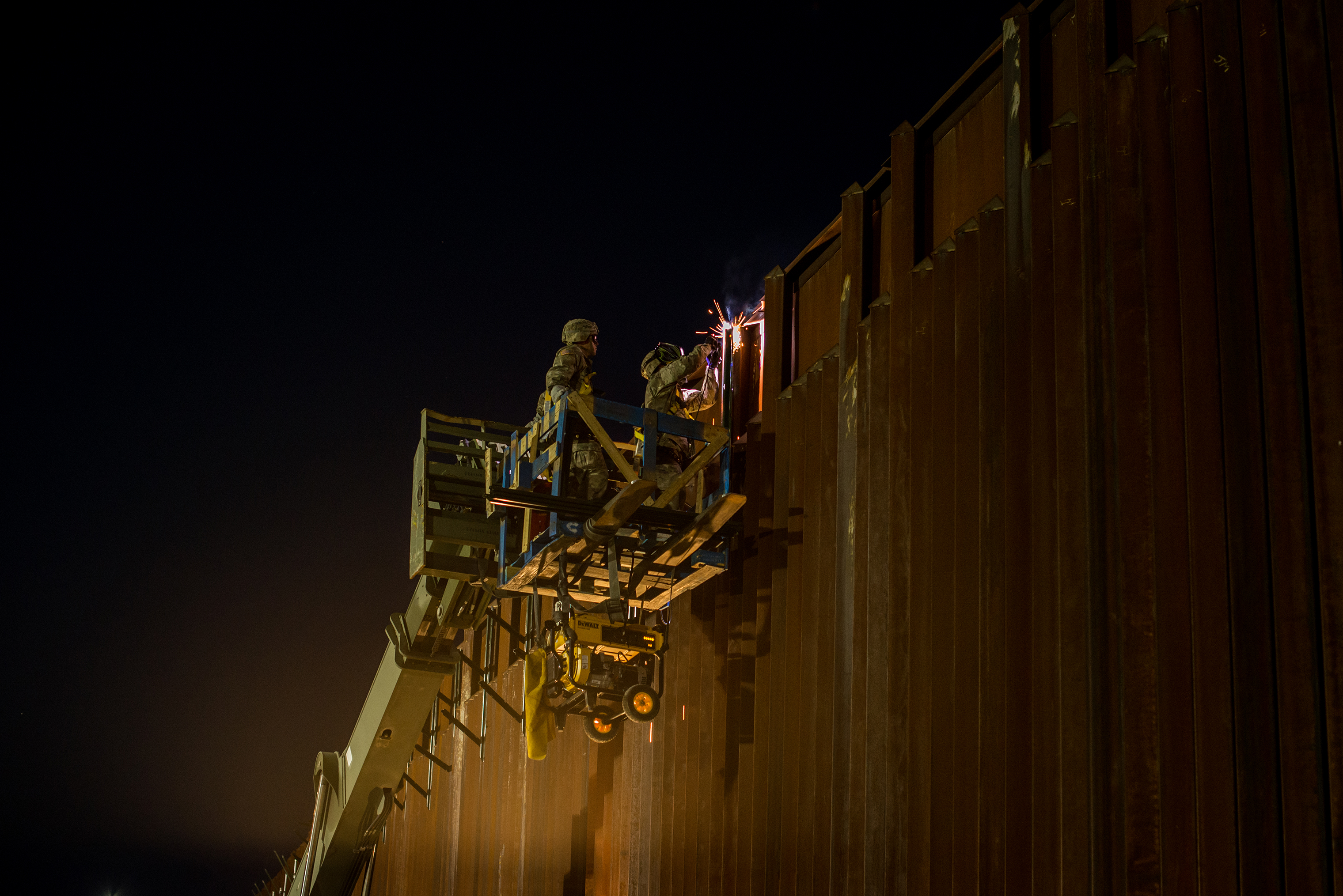 Soldiers of the 104th Engineer Construction Company weld brackets for concertina wire along the border wall. (Meridith Kohut for TIME)