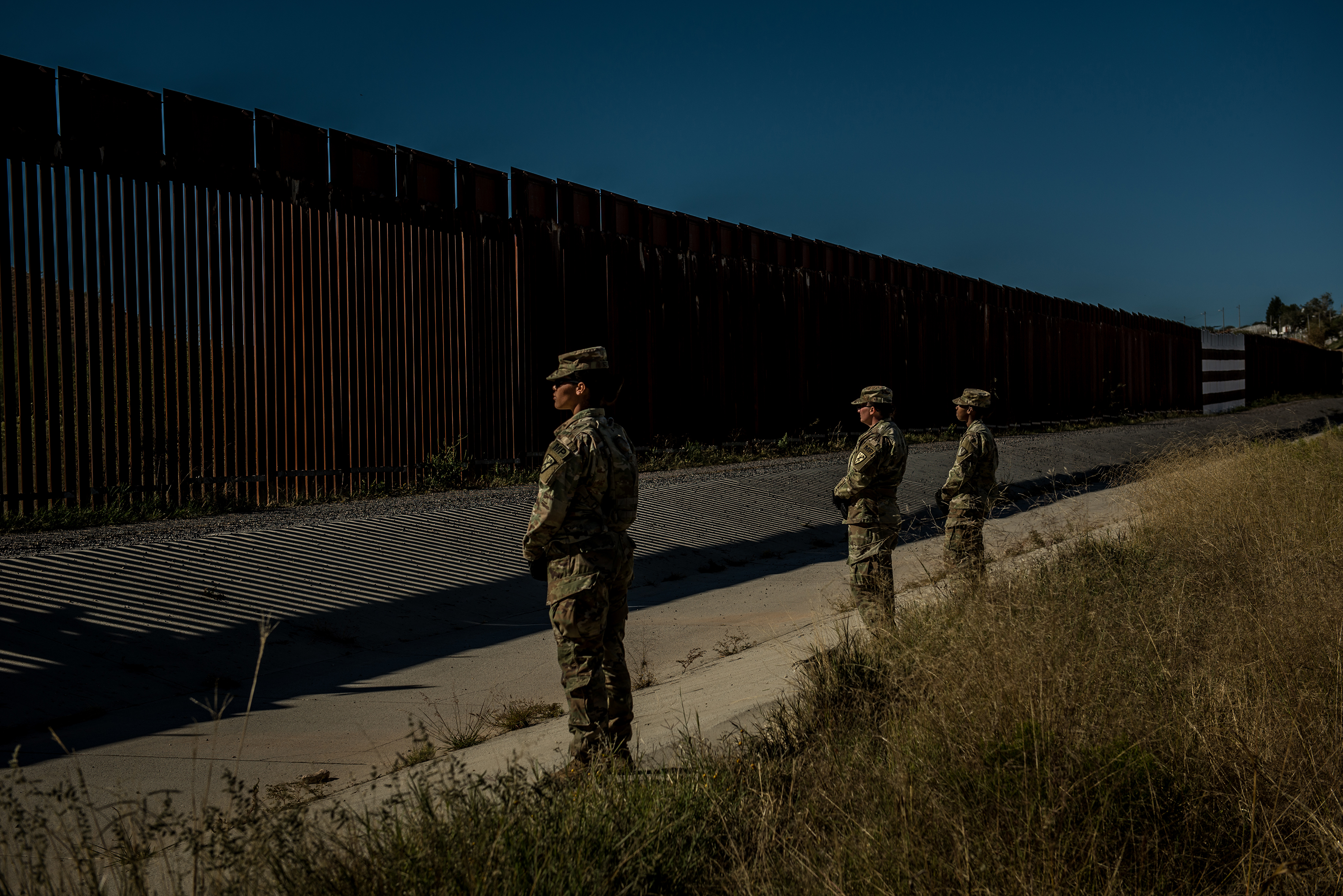 Military police stand guard as other members of the 104th Engineer Construction Company  work to heighten security of the border wall. (Meridith Kohut for TIME)