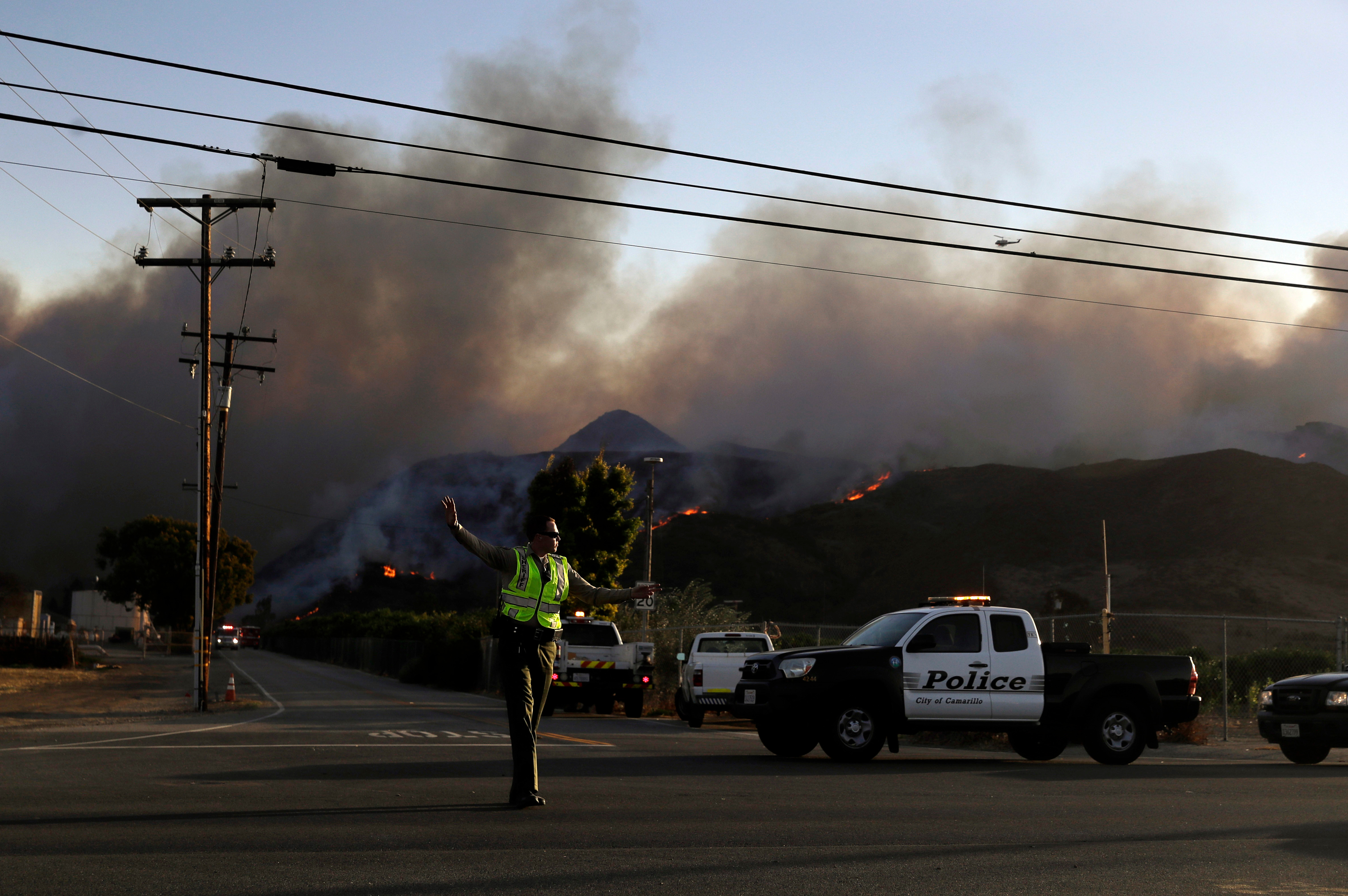 A police officer mans a checkpoint in front of an advancing wildfire, near Newbury Park, Calif. onNov. 9, 2018. The Ventura County Fire Department has also ordered evacuation of some communities in the path of the fire, which erupted a few miles from the site of Wednesday night's deadly mass shooting at a Thousand Oaks bar. (Marcio Jose Sanchez—AP/REX/Shutterstock)