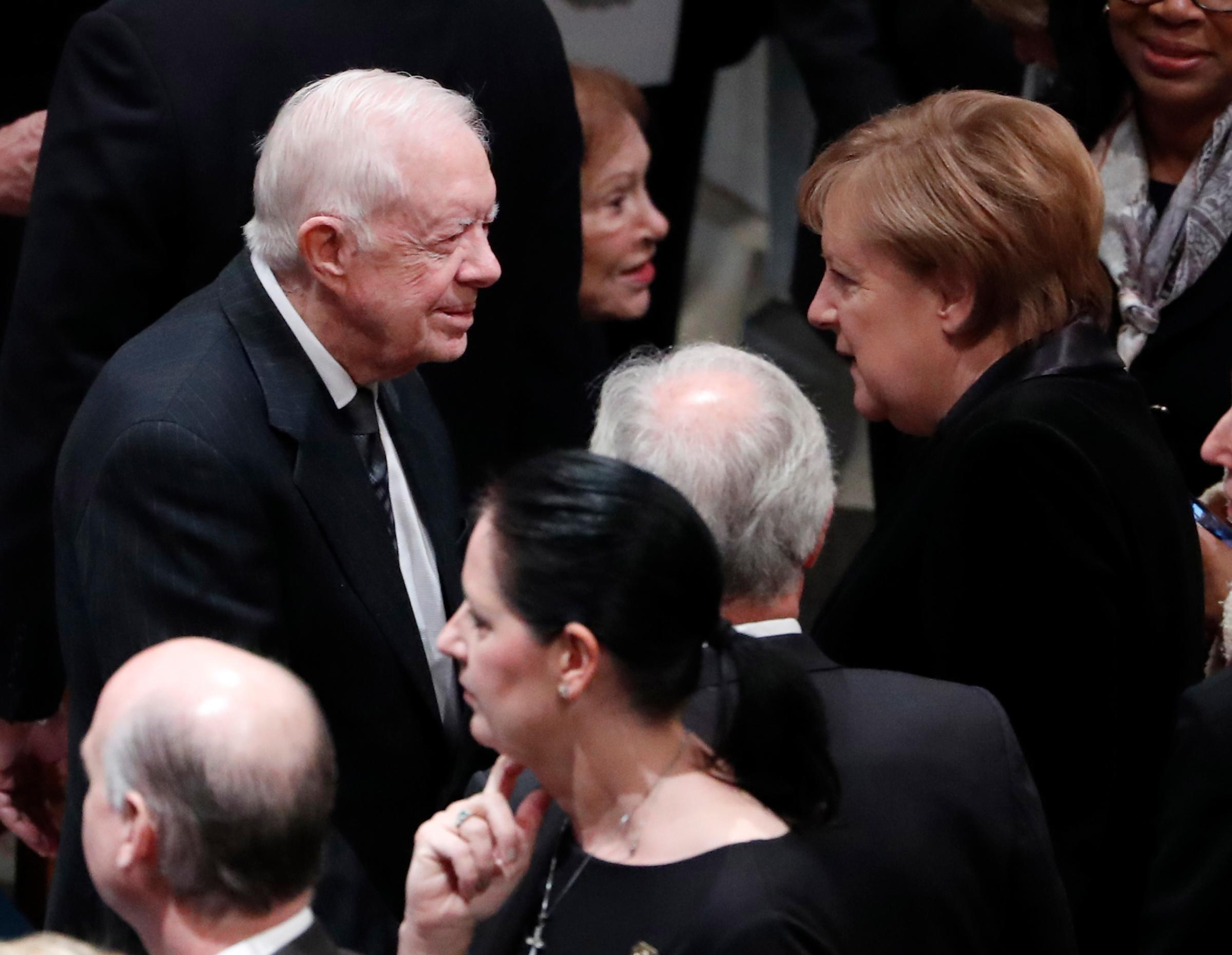 Former United States President Jimmy Carter talks with German Chancellor Angela Merkel as they attend the funeral of former United States President George H. W. Bush at the National Cathedral