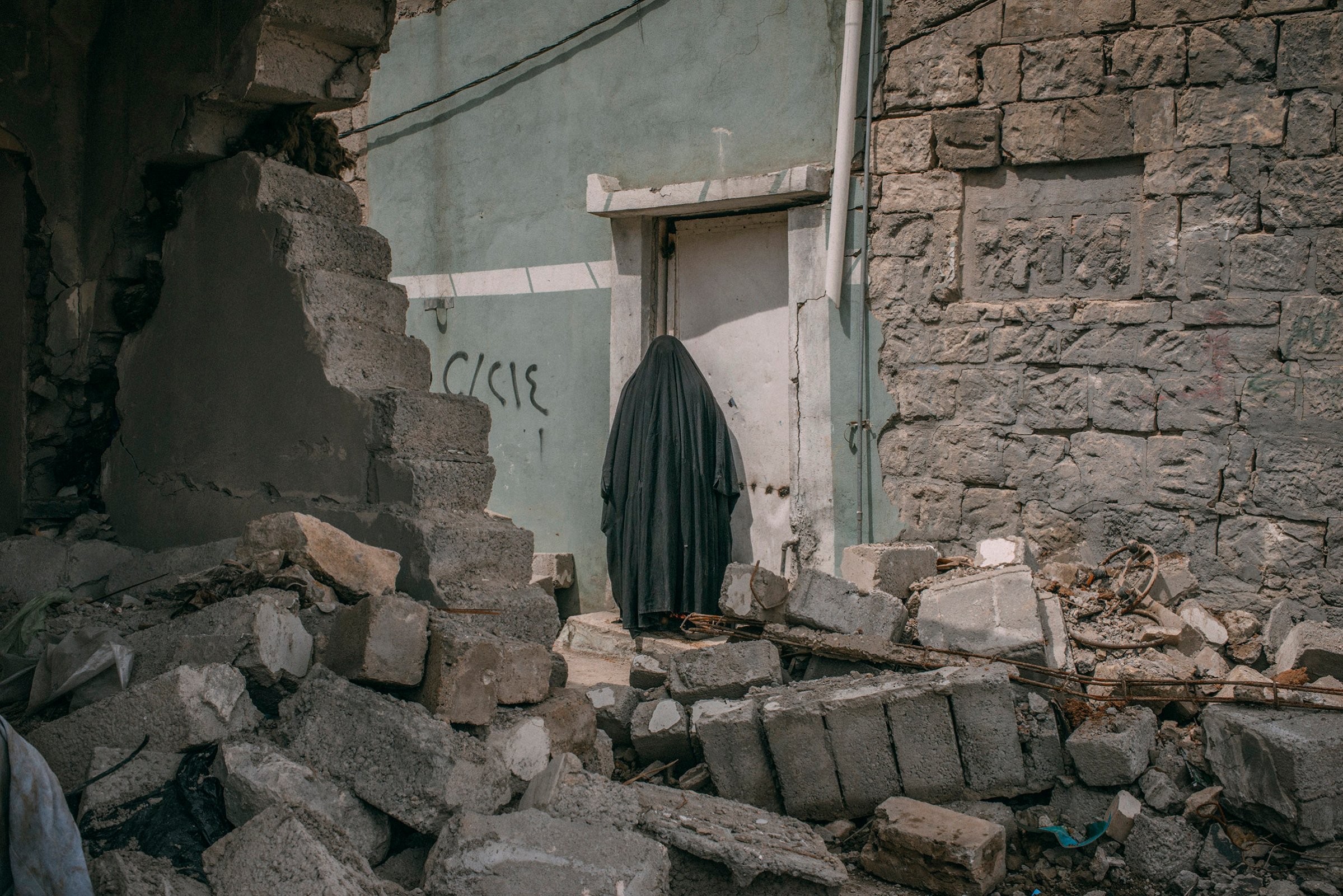 A woman stands among buildings damaged by airstrikes in southwest Mosul on April 3, 2017