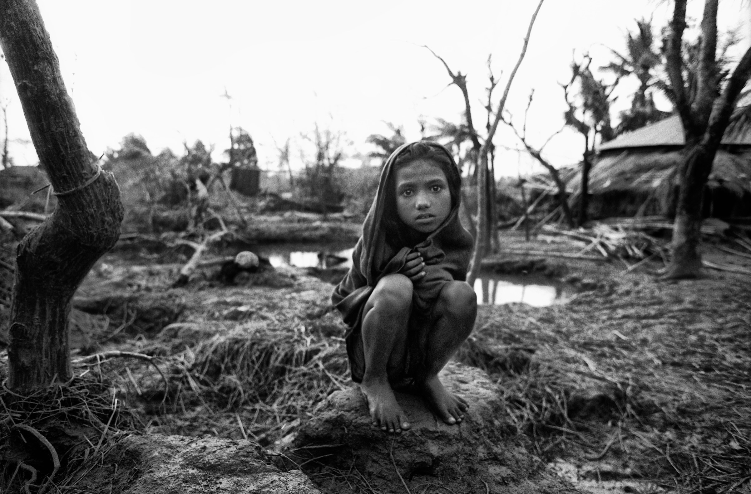 A girl crouches near the remains of her home in the aftermath of a deadly storm in Anwara, Chittagong, Bangladesh, 1991. (Shahidul Alam—Drik)