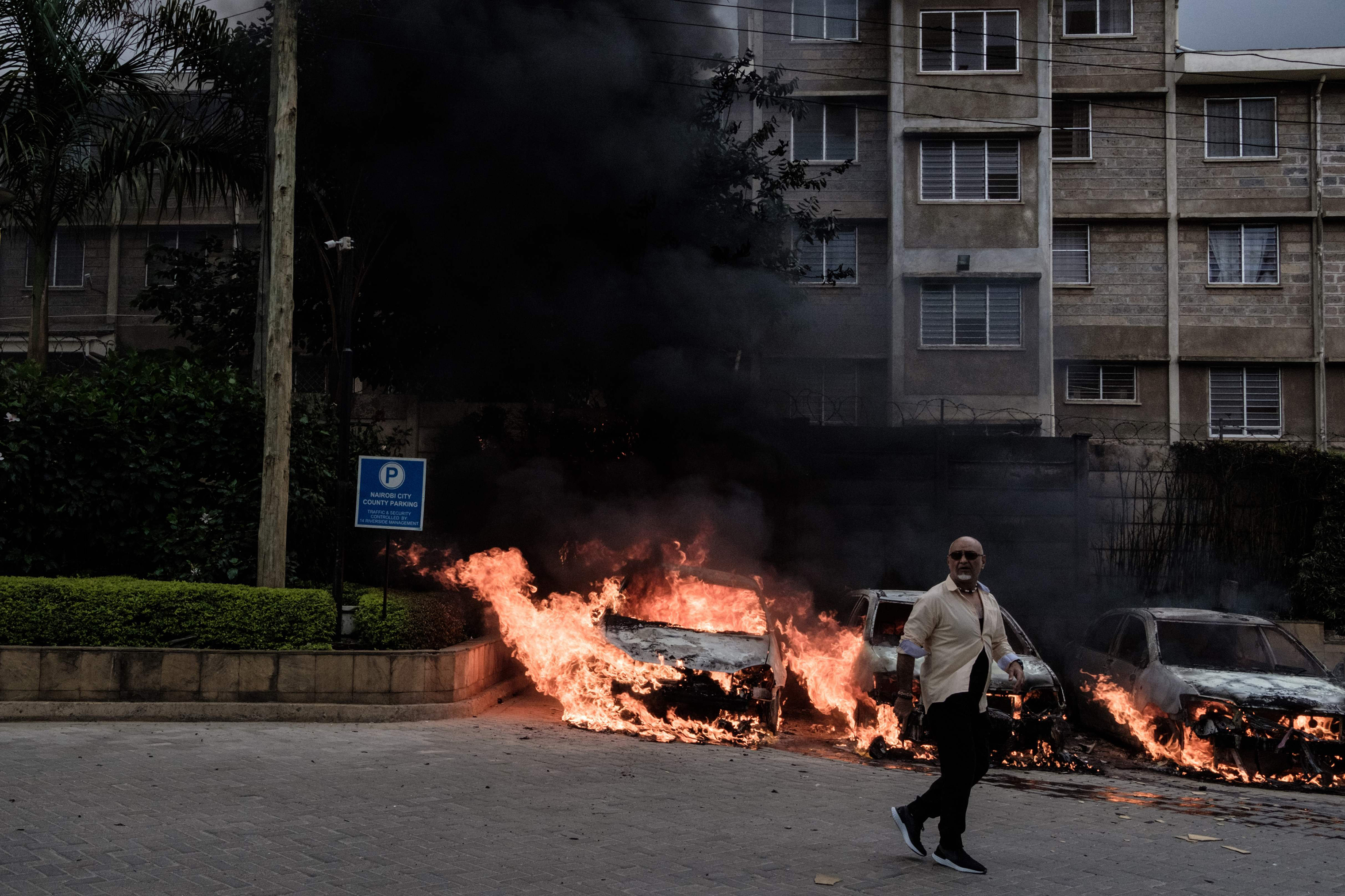 A man passes in front of burning cars that exploded at the entrance of dusitD2 hotel in Nairobi. (Kabir Dhanji—AFP/Getty Images)