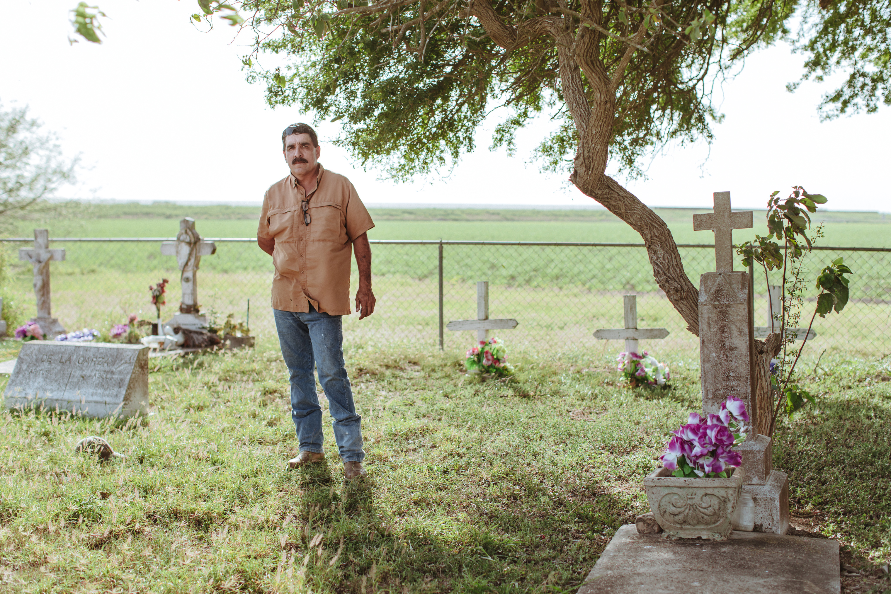 Charlie Vasquez at his family cemetery standing in front of the border fence in Donna, Texas. (Elliot Ross)