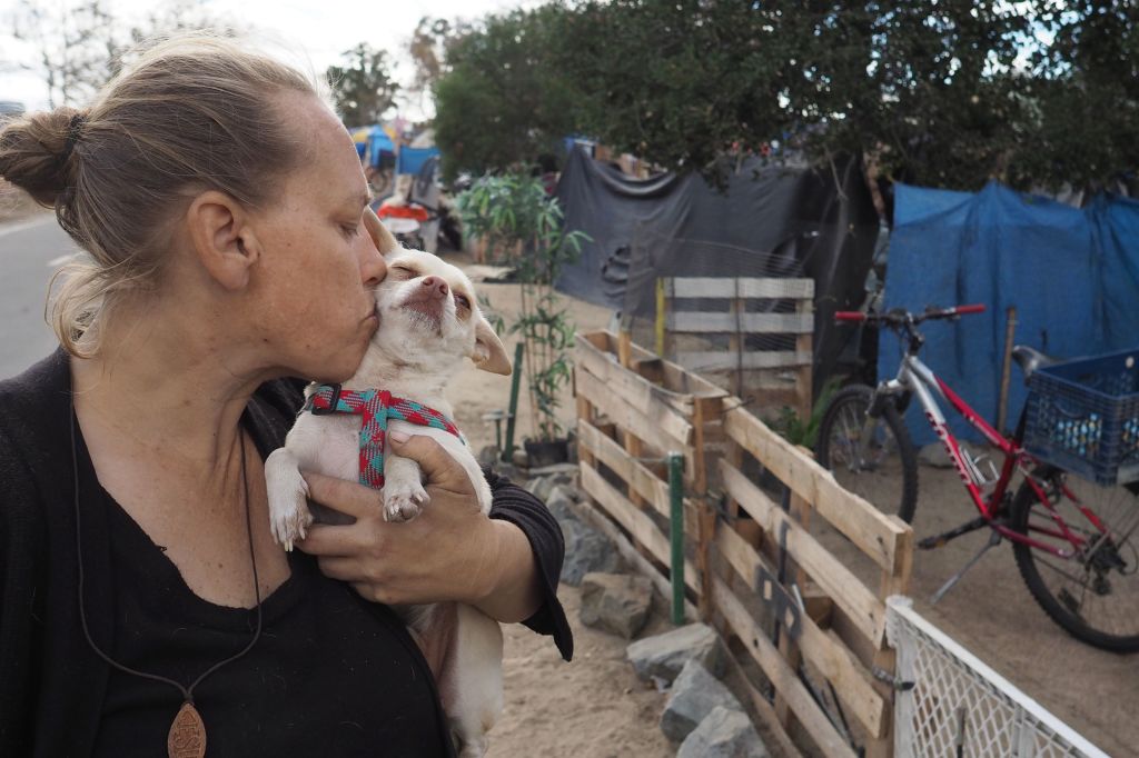 Homeless encampment resident Tammy Schuler kisses one of her pet dogs  beside a row of tents and tarps that line the Santa Ana River bicycle path, near Angel Stadium in Anaheim, California, January 25, 2018. (Robyn Beck&mdash;AFP/Getty Images)