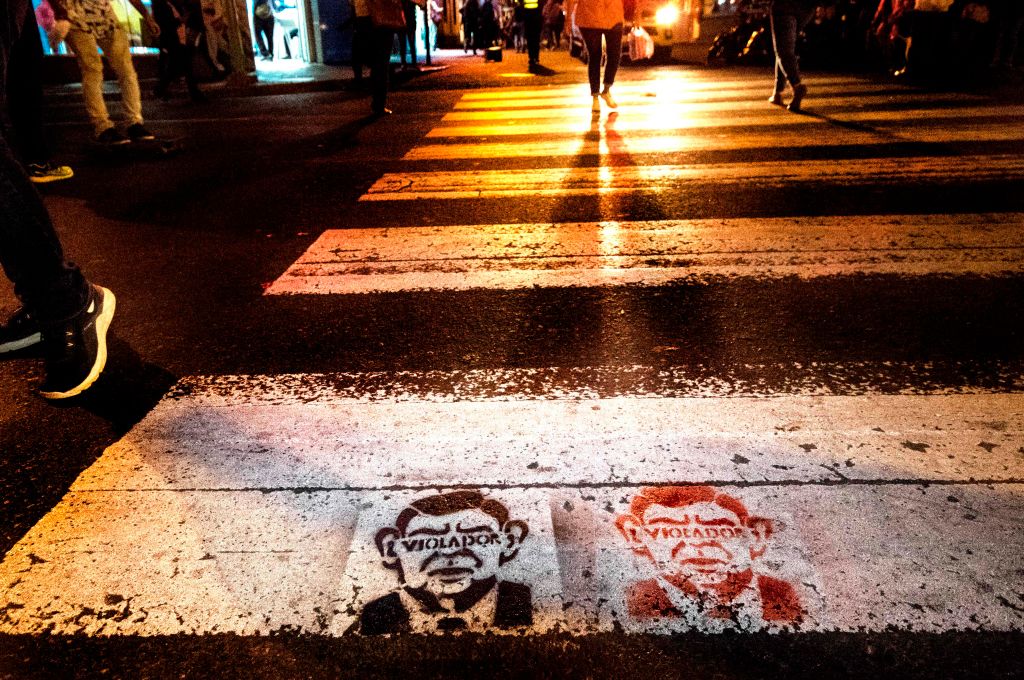 People walk through a pedestrian zone where graffiti that reads 