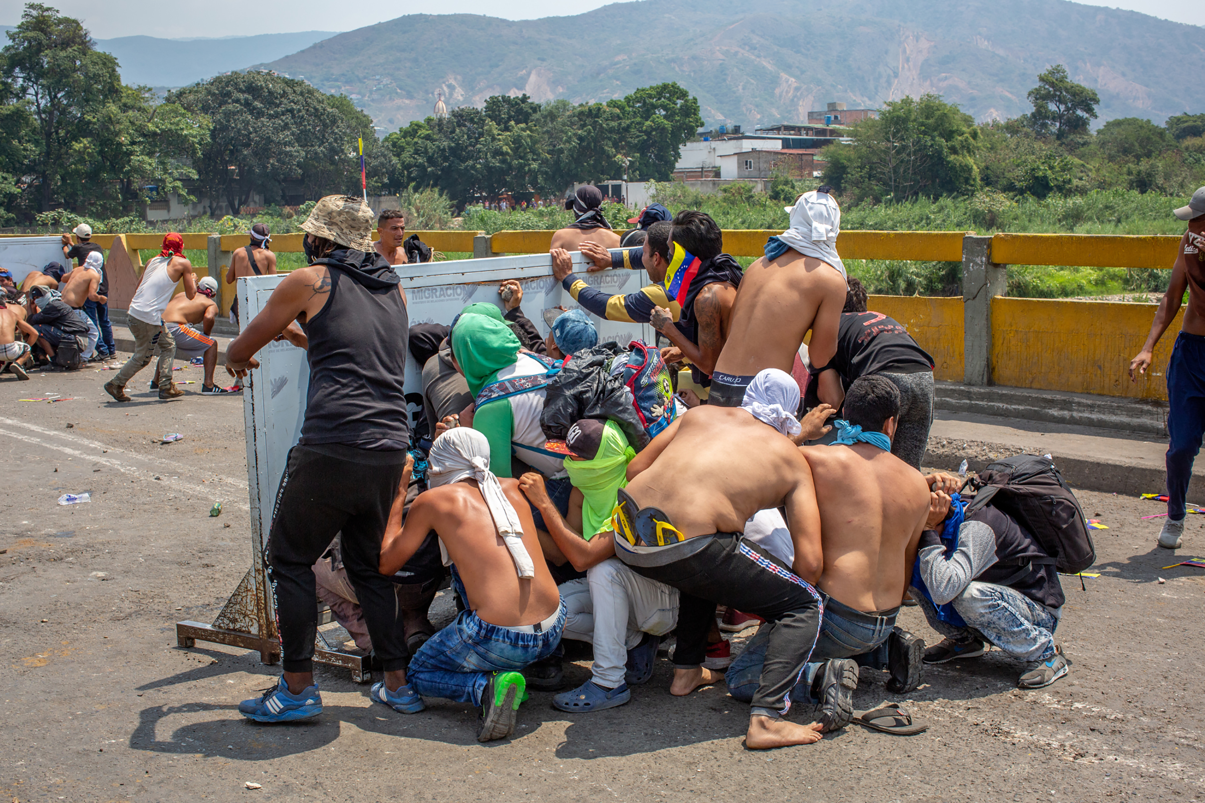 A group of demonstrators take cover during a clash with Venezuelan national police officers on the bridge. (Photograph by TIME)