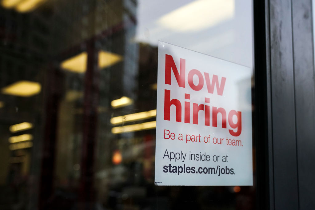 A 'now hiring' sign hangs on the door of a Staples store