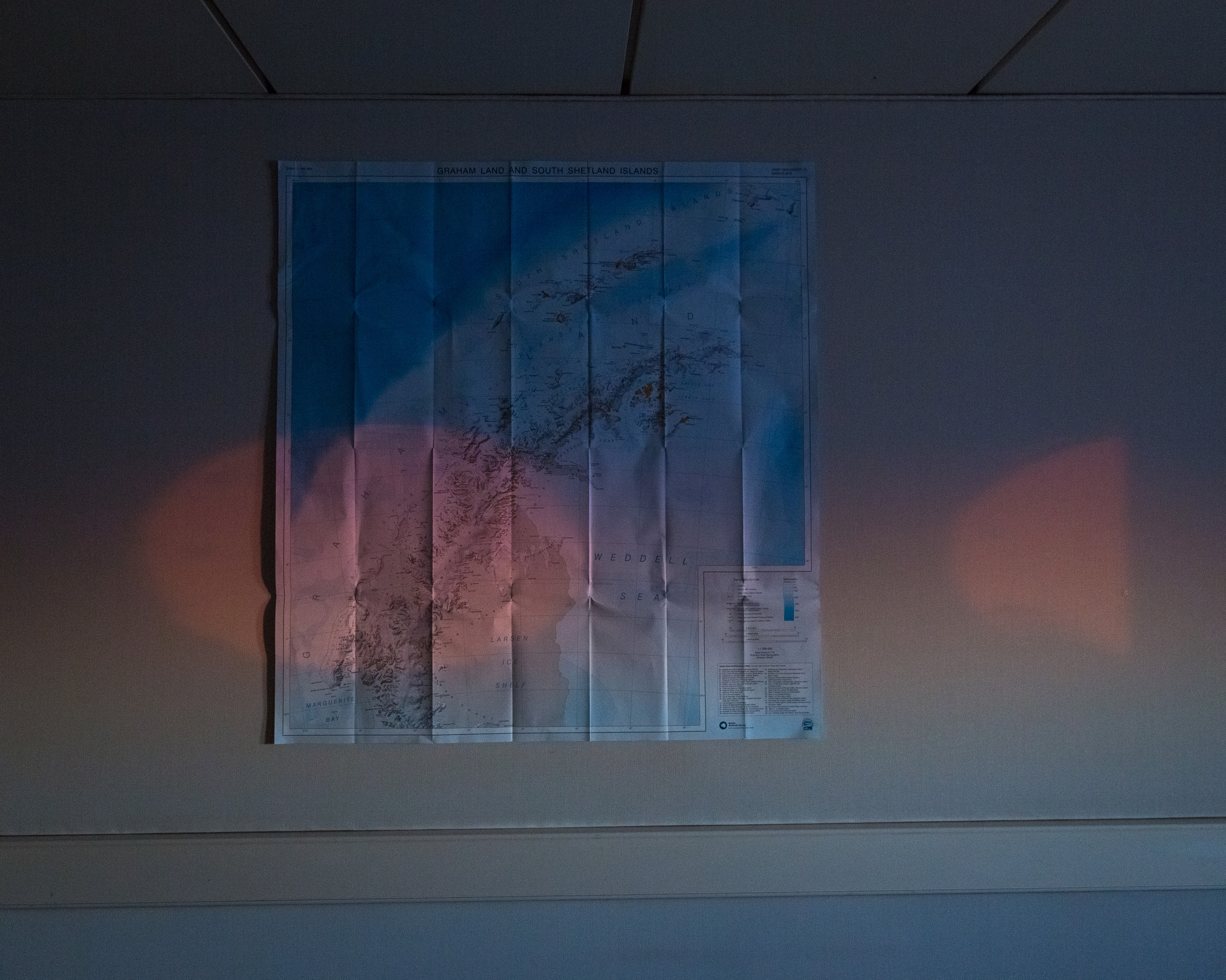 An Antarctic sunset glows through the portholes of a bedroom. On the wall is a map of the Antarctic Peninsula.
