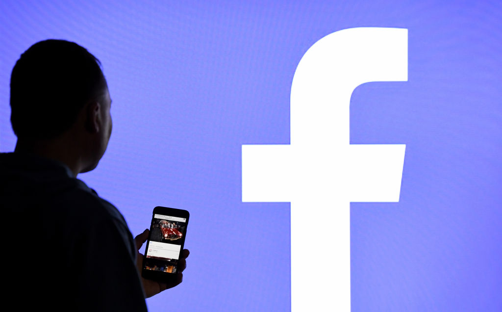 Man Stands in Front of Facebook Logo Screen