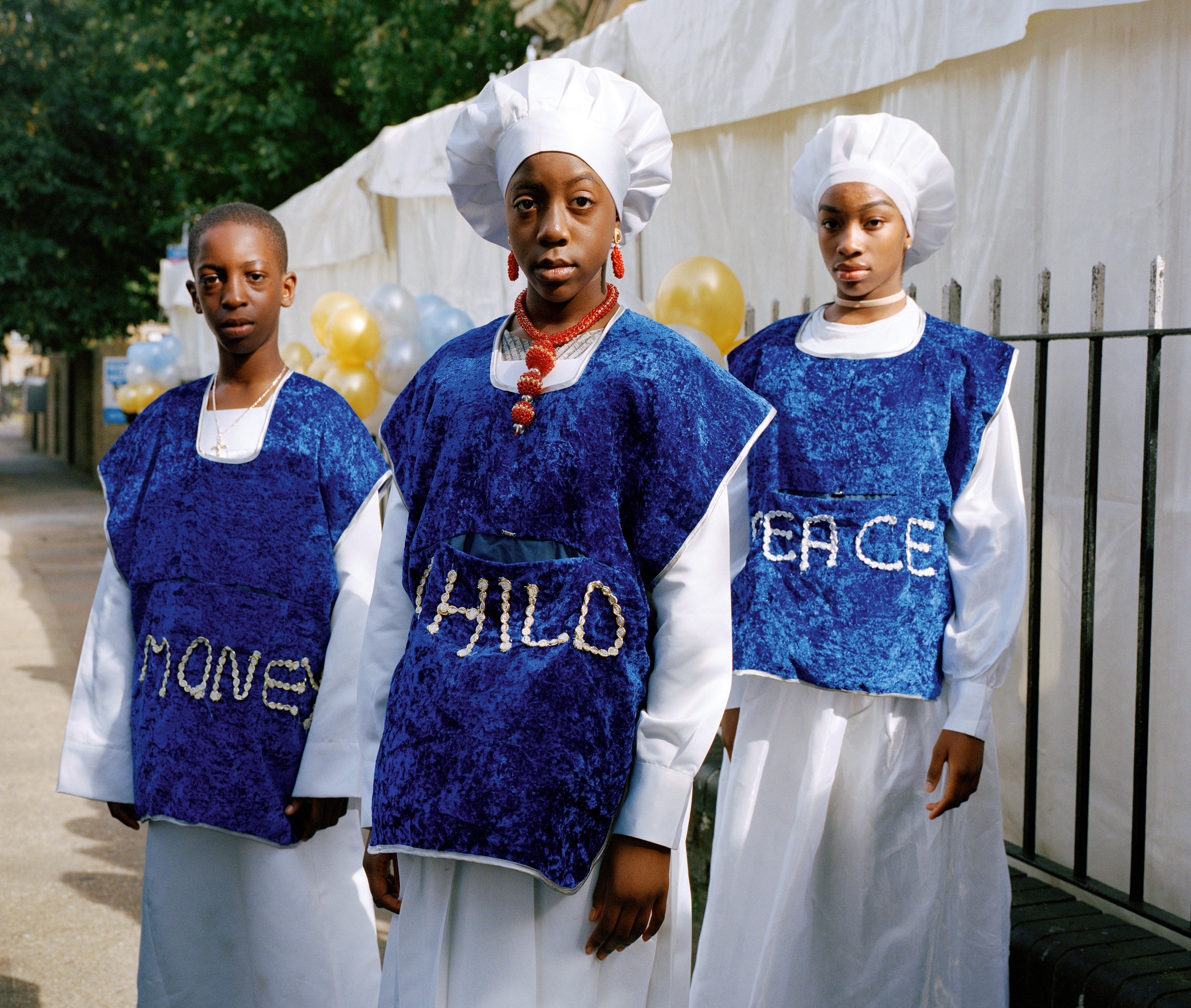 Josiah, Bukky and Lauren stand outside church on children’s anniversary service wearing clothing that reads Money, Child, Peace as they collect donations from their fellow congregants for charity. (Sophie Green)