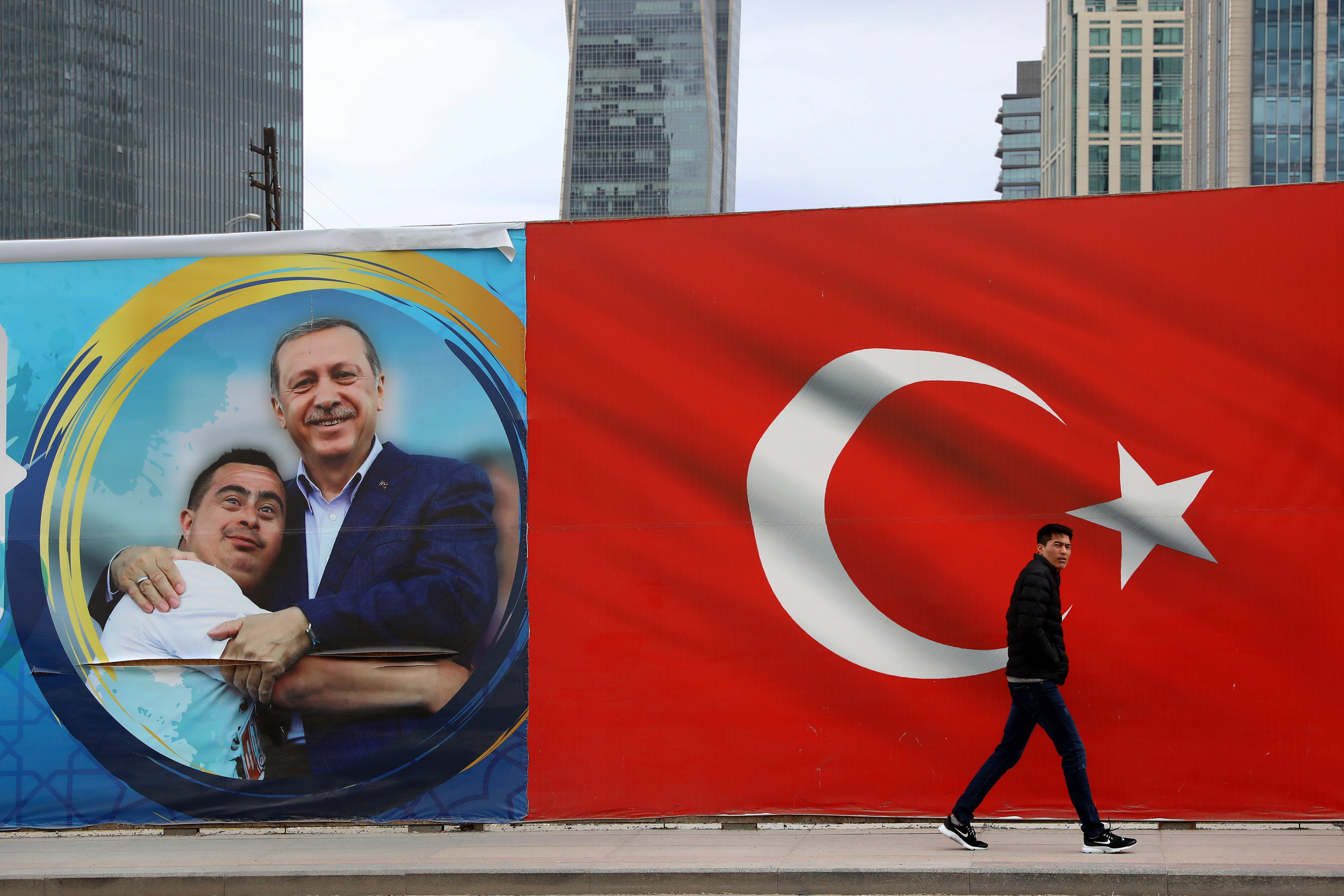 A man walks by a Turkish flag and a poster showing the Turkey's President Recep Tayyip Erdogan with a boy in Ankara, Turkey on Mar. 31, 2019. (Ali Unal&mdash;AP)