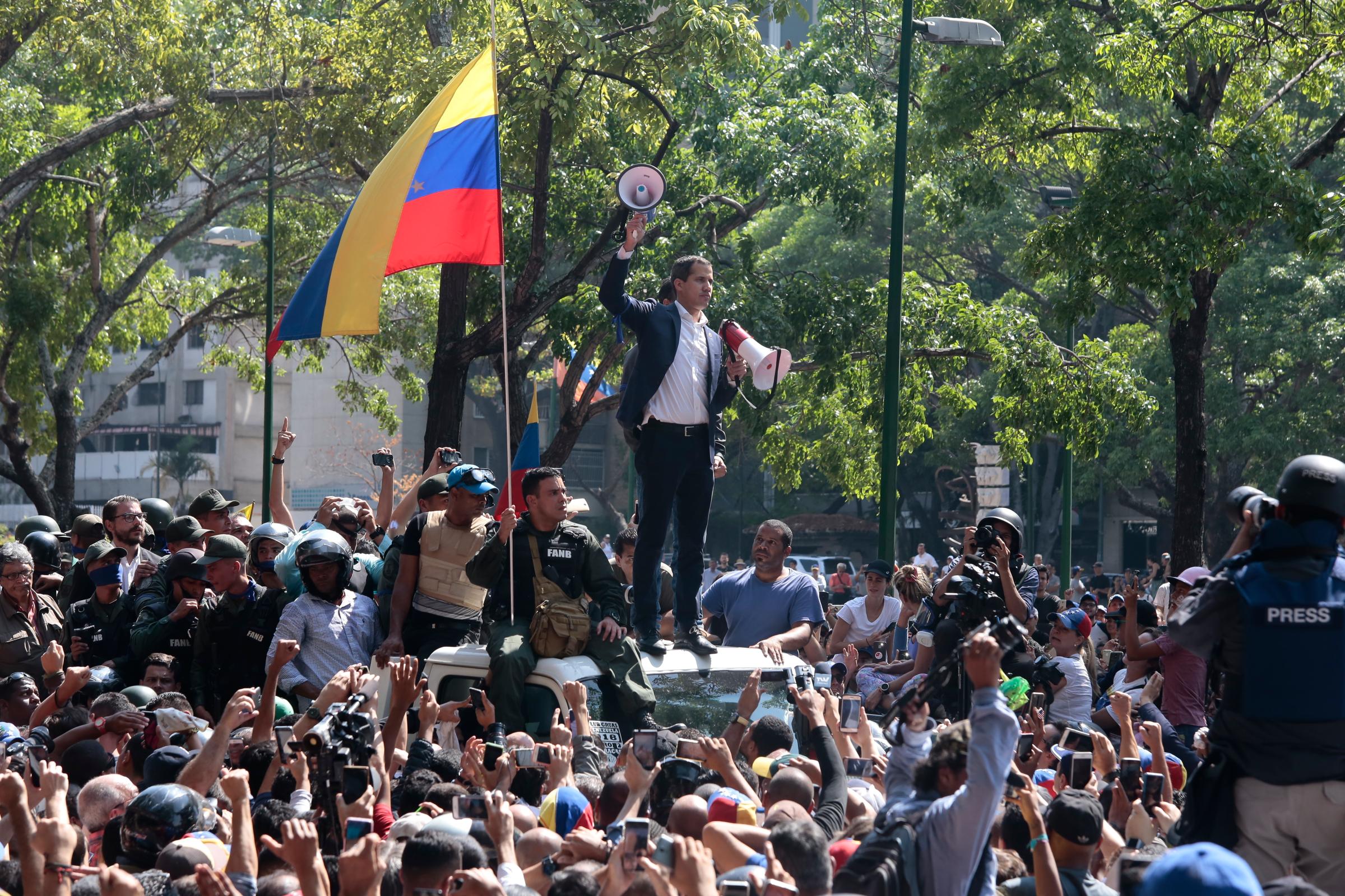 Juan Guaido, self-proclaimed interim president of Venezuela, stands with two megaphones in his hands surrounded by soldiers and civilians at Plaza Altamira