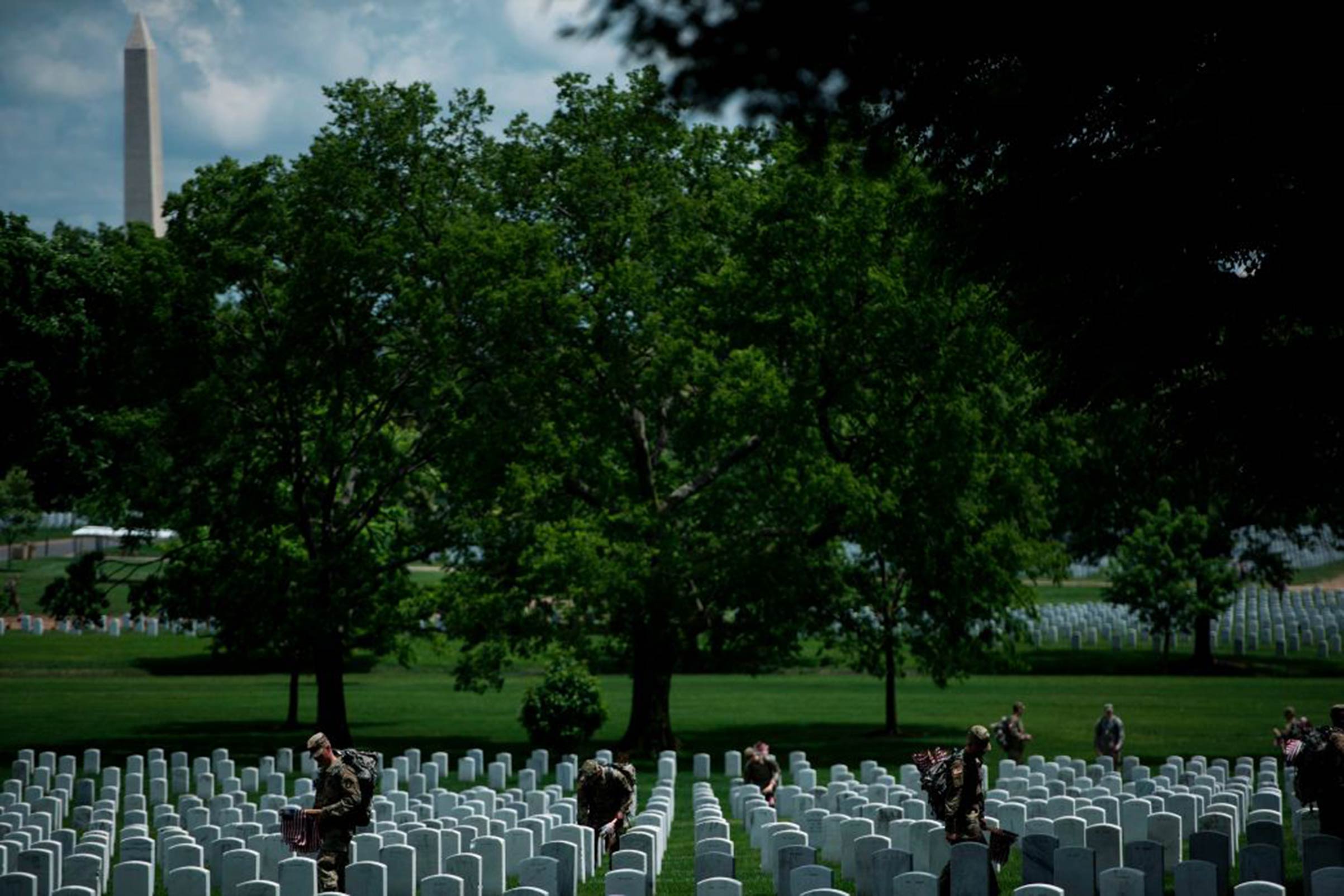 Soldiers in the Old Guard place flags at graves in Arlington National Cemetery during 