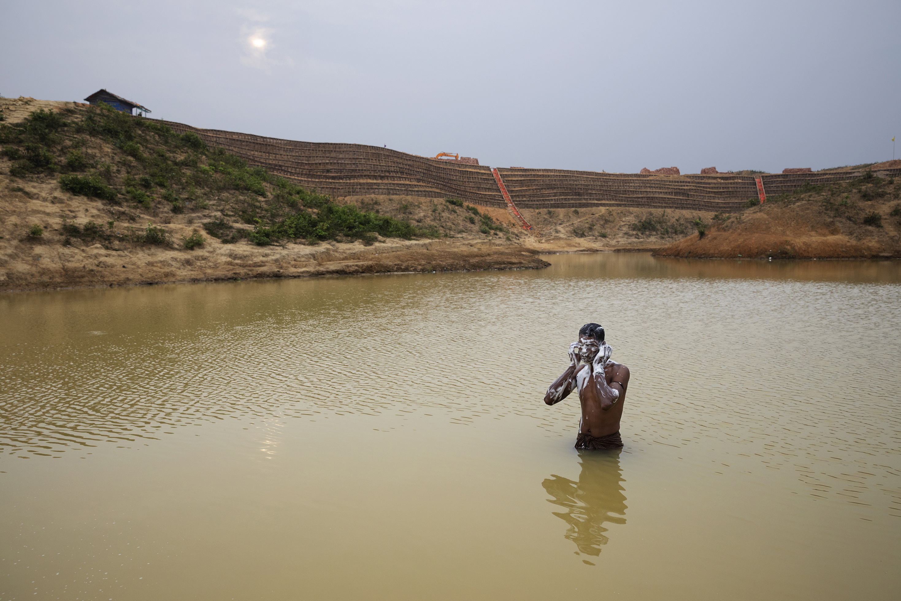 A man bathes in a man-made pond near the camp where he lives. Behind him is the construction of the Camp 20 Extension. (James Nachtwey for TIME)