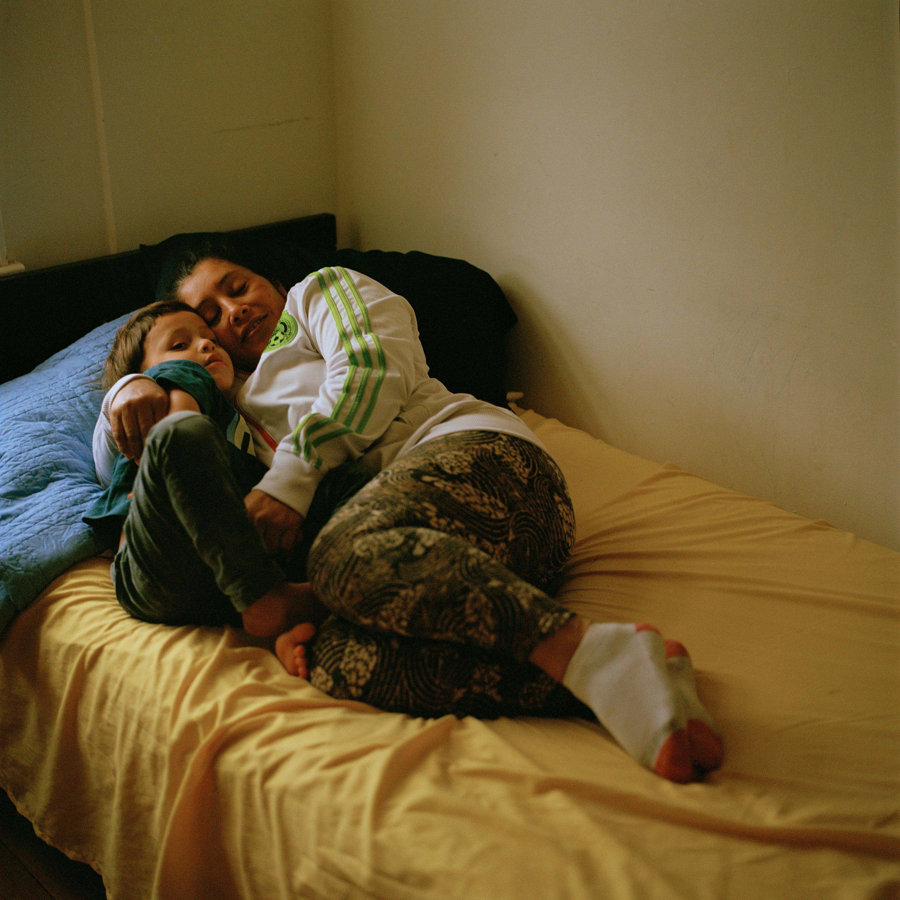 Maria, right, lays in bed with Enoc for an afternoon nap on March 25. Castro sleeps at home when her other children are at school because she suffers from high blood pressure, often causing strong headaches, she says: “My [ankle] bracelet hurts me and I want to get it off, but at the court they said they would remove it in six months.” (Federica Valabrega)