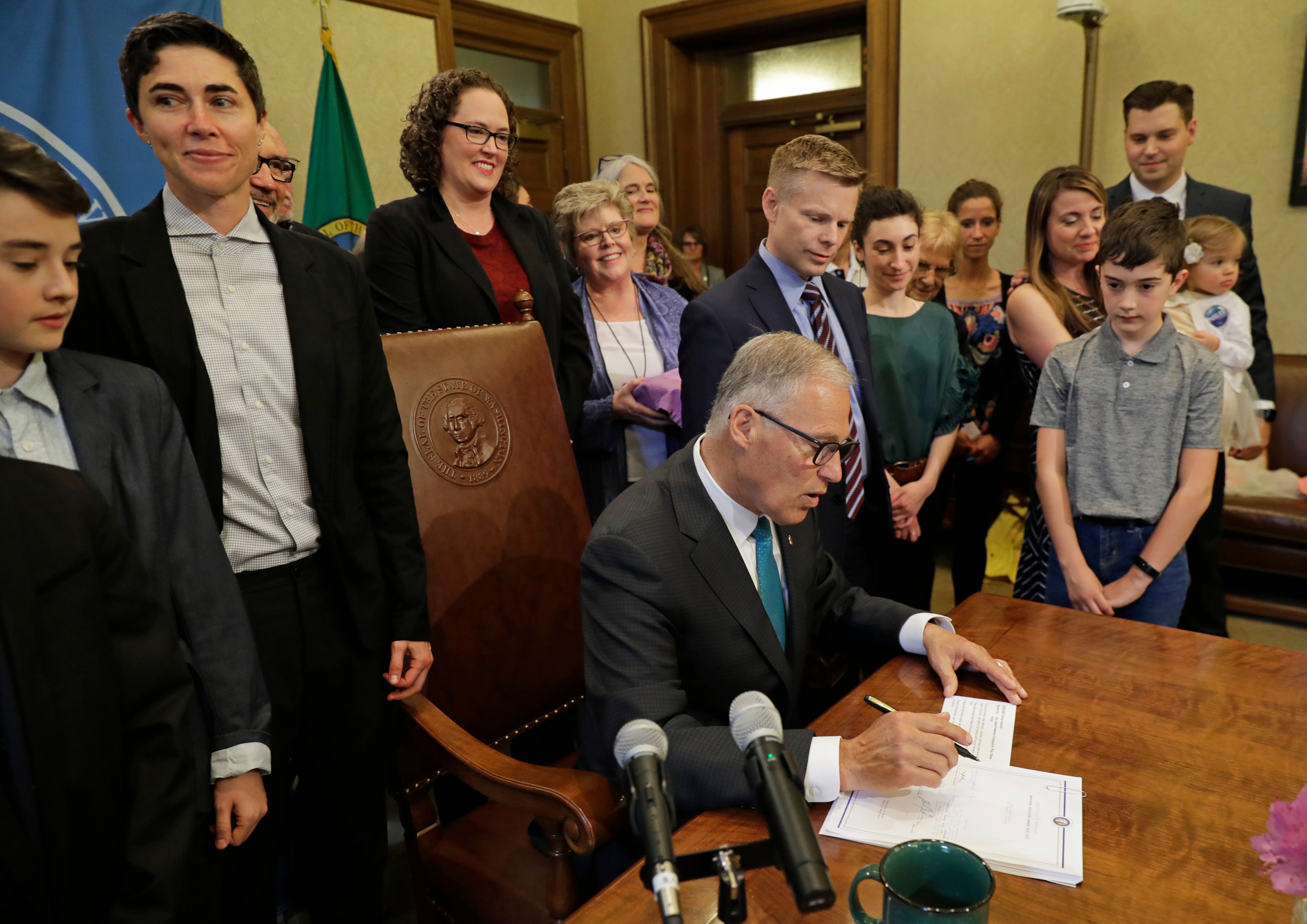 Katrina Spade, upper left, the founder and CEO of Recompose, looks on May 21, 2019, as Washington Gov. Jay Inslee, center, signs a bill into law that allows licensed facilities to offer 'human composting' services. (Ted S. Warren/AP)