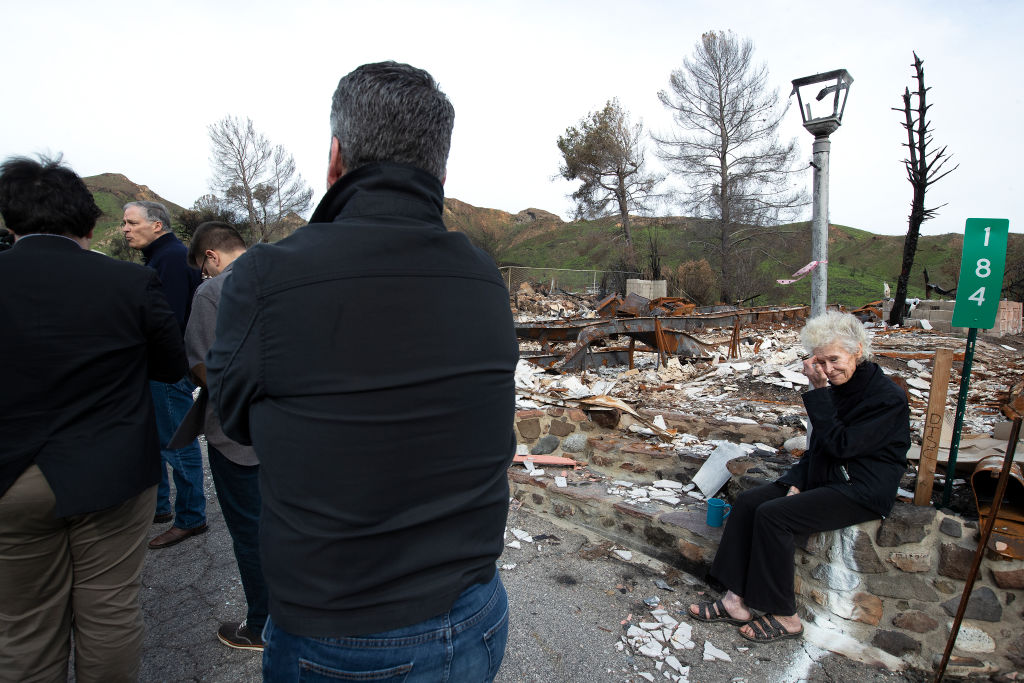 Marsha Maus, 75, right, a 15-year resident of Seminole Springs Mobile Home Park in Agoura Hills, sits next to a destroyed home as Gov. Jay Inslee of Washington talks with the media while touring Seminole Springs after devastating wildfires on March 11, 2019 in Agoura Hills, California. (Mel Melcon—LA Times via Getty Images)