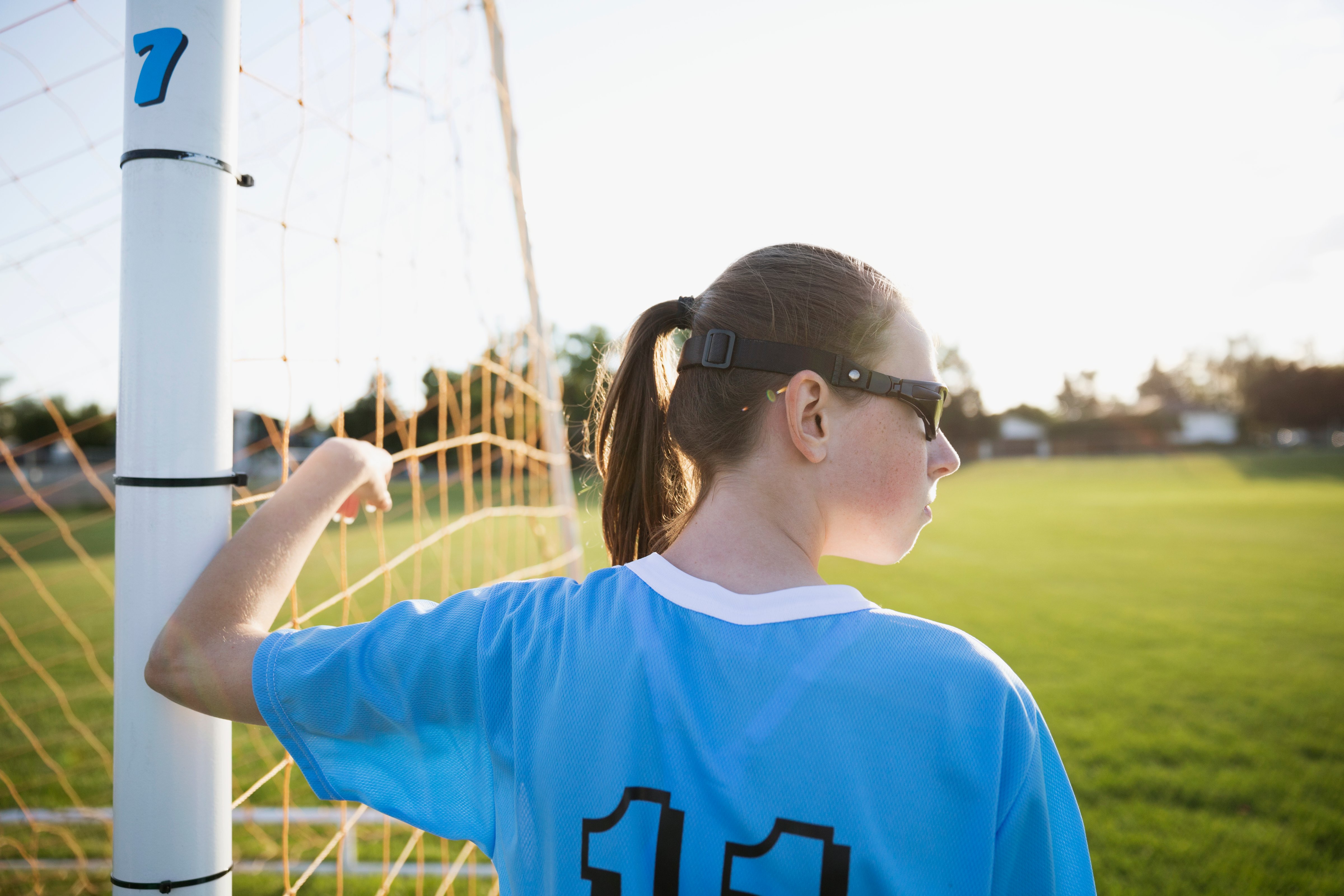 Middle school girl soccer player leaning on goal net post looking away