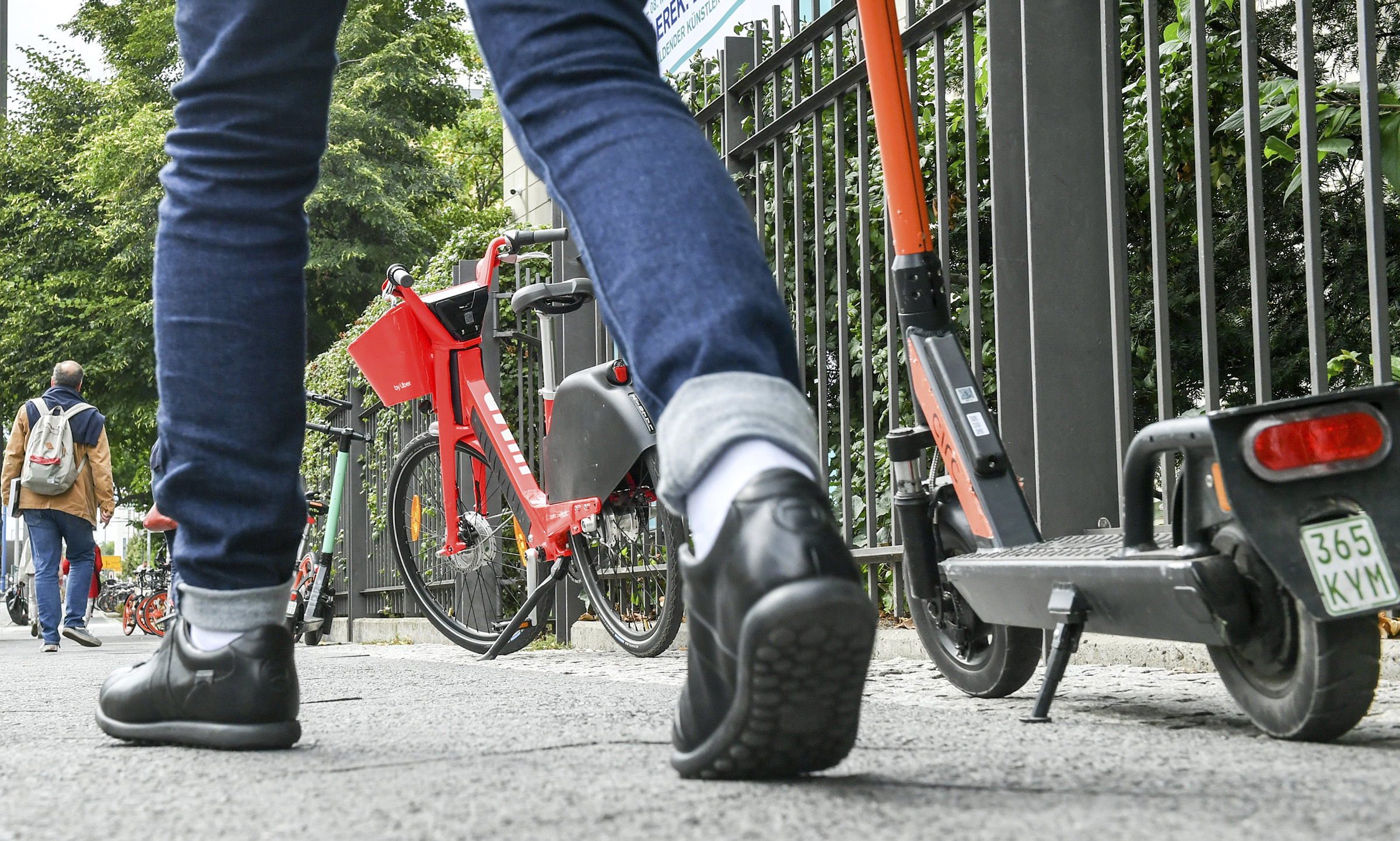Numerous e-bikes and e-scooters stand on a footpath where pedestrians are on the move. (Jens Kalaene—Jens Kalaene/picture-alliance/dp/AP)