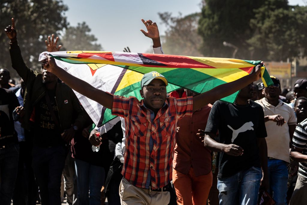 A man holding Zimbabwe's national flag walks with other protesters as they march in the streets of Harare on August 16, 2019. Riot police in Zimbabwe fired teargas and beat demonstrators on August 16 during a crackdown on opposition supporters who have taken to Harare's streets despite a protest ban. (ZINYANGE AUNTONY—AFP/Getty Images)