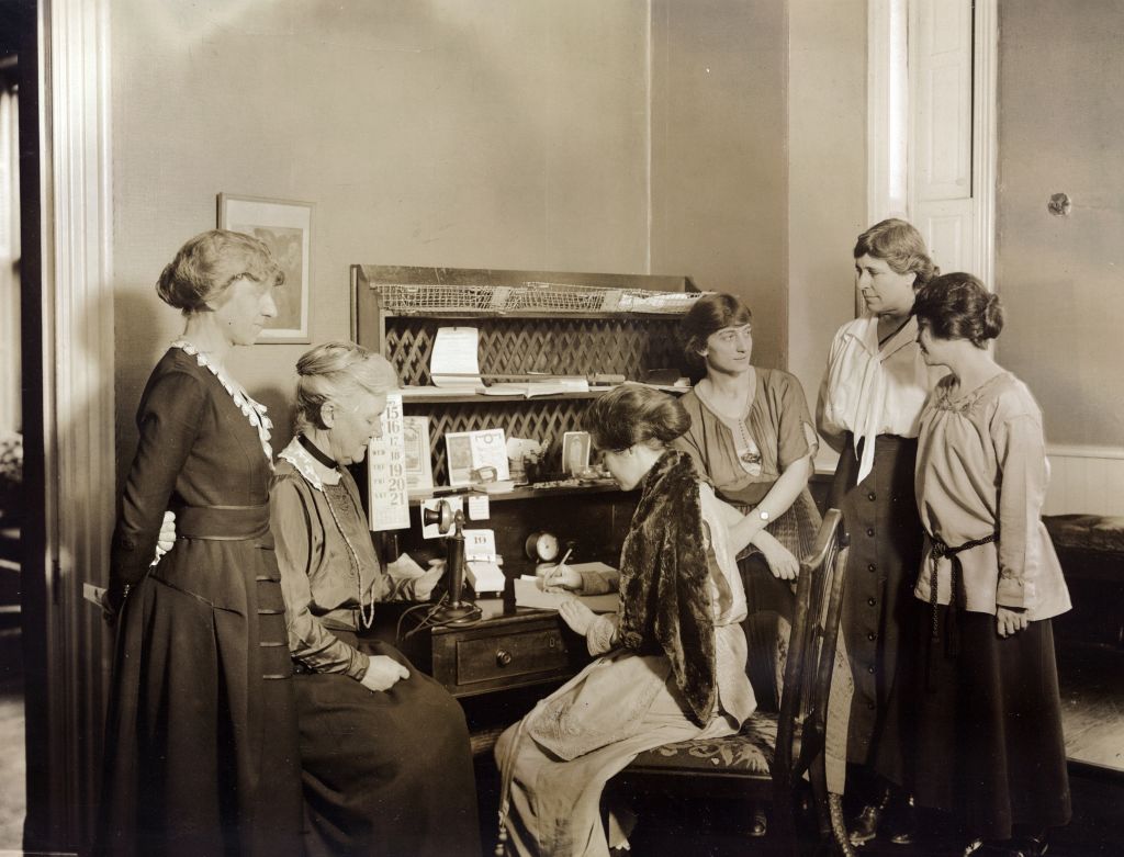 Six National Woman's Party members gathered around a desk at National Woman's Party headquarters. Left to right: Mabel Vernon, Dora Lewis, Alice Paul (seated), Florence Brewer Boeckel, Abby Scott Baker, and Anita Pollitzer. Feb. 1921. (Photo 12—Universal Images Group via Getty)