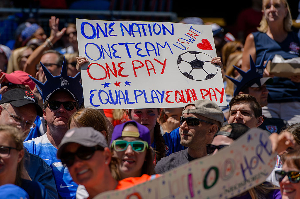A fan holds an equal pay sign at a USWNT game
