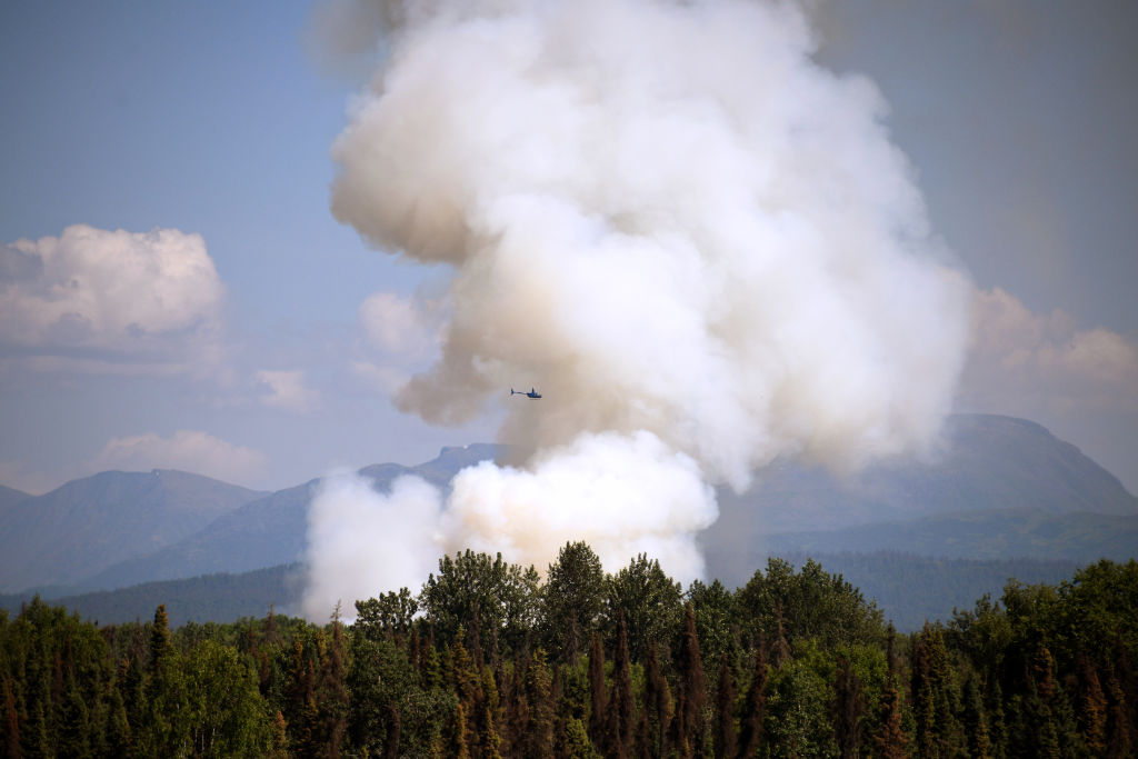 A helicopter passes by as smoke rises from a wildfire on July 3, 2019 south of Talkeetna, Alaska near the George Parks Highway. (Lance King&mdash;Getty Images)