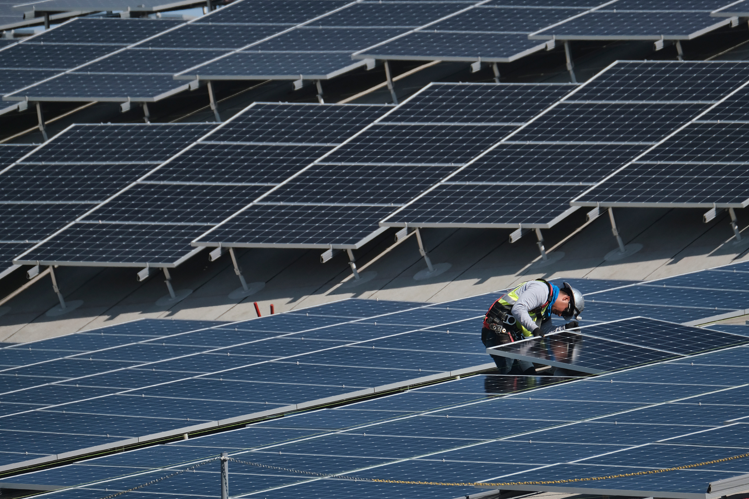 In this Aug. 8, 2019 photo a worker helps to install solar panels onto a roof at the Van Nuys Airport in the Van Nuys section of Los Angeles. (Richard Vogel—AP)